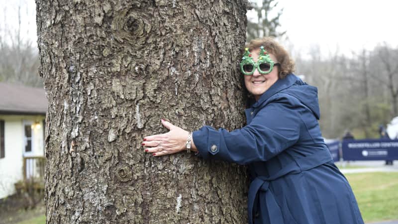 Carol Schultz, wearing an appropriate pair of sunglasses, gives her beloved 77-foot Norway spruce one last squeeze before it's cut down.