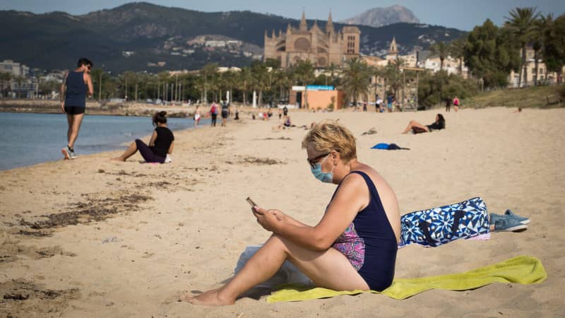 A woman wearing a face mask sits at the Can Pere Antoni Beach in Palma de Mallorca on May 25, 2020
