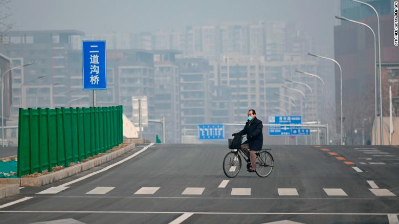 A man wearing a face mask rides his bicycle along an empty street in Beijing on February 12, 2020.