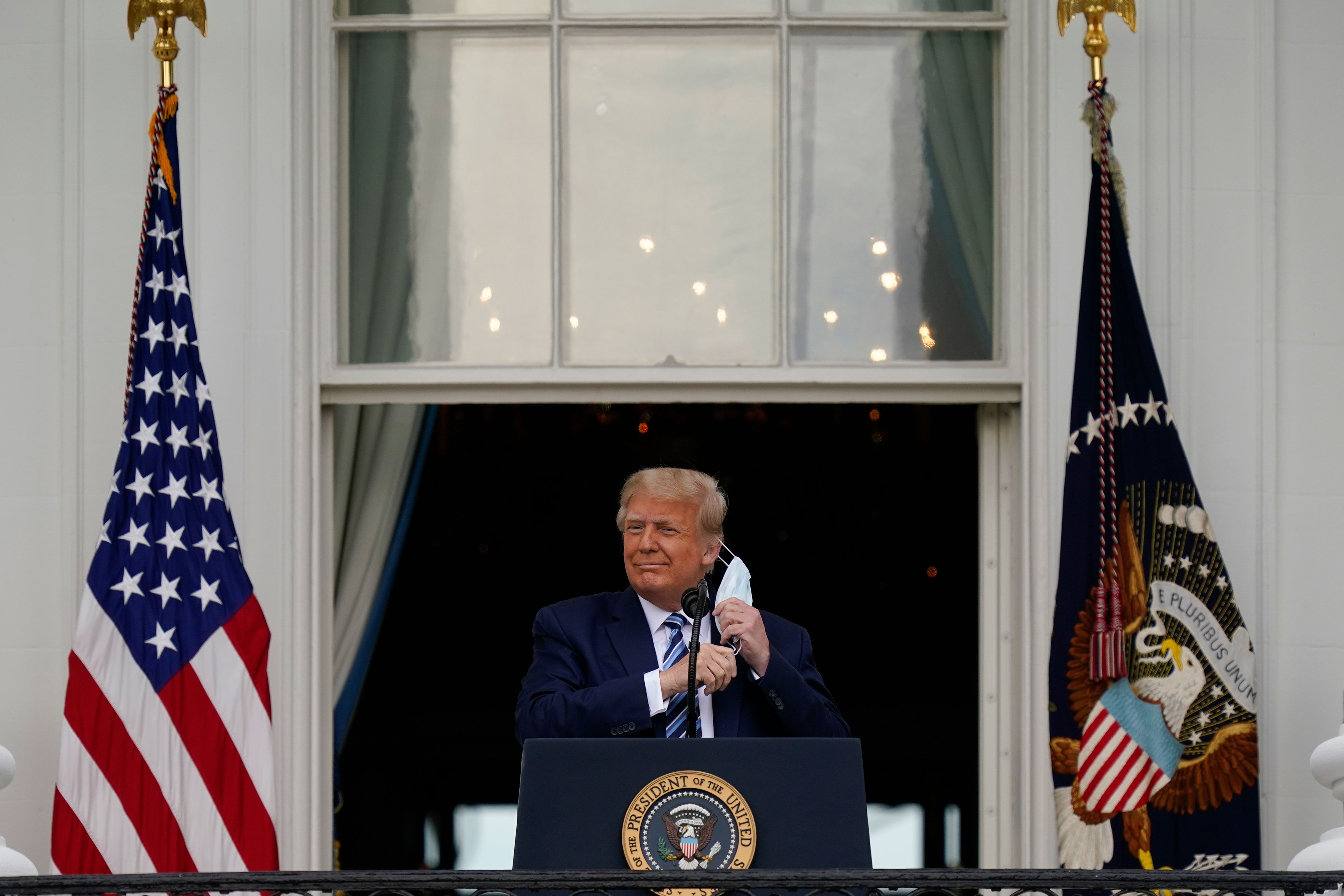 President Donald Trump removes his face mask before speaking to supporters at the White House on October 10.