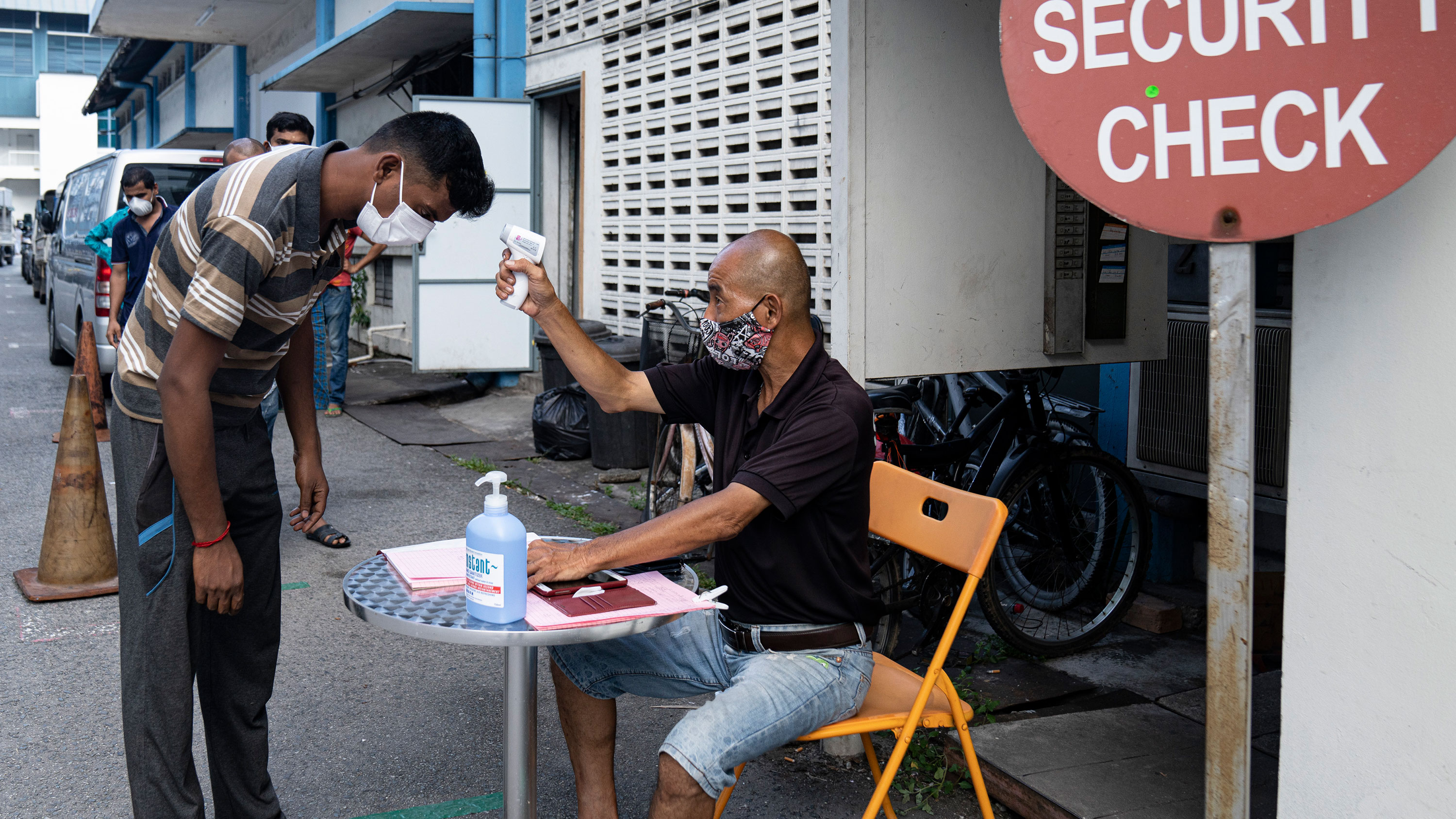 A security guard checks the temperature of a migrant worker leaving a dormitory on April 17, in Singapore.