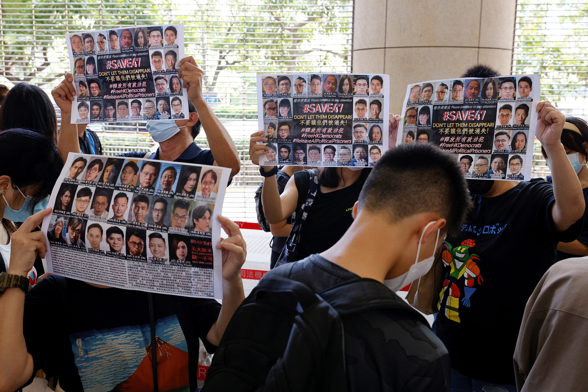 Supporters hold up placards among people queuing up at the West Kowloon Magistrates’ Courts for a hearing of 47 pro-democracy activists charged with violating the national security law in Hong Kong on July 8, 2021.