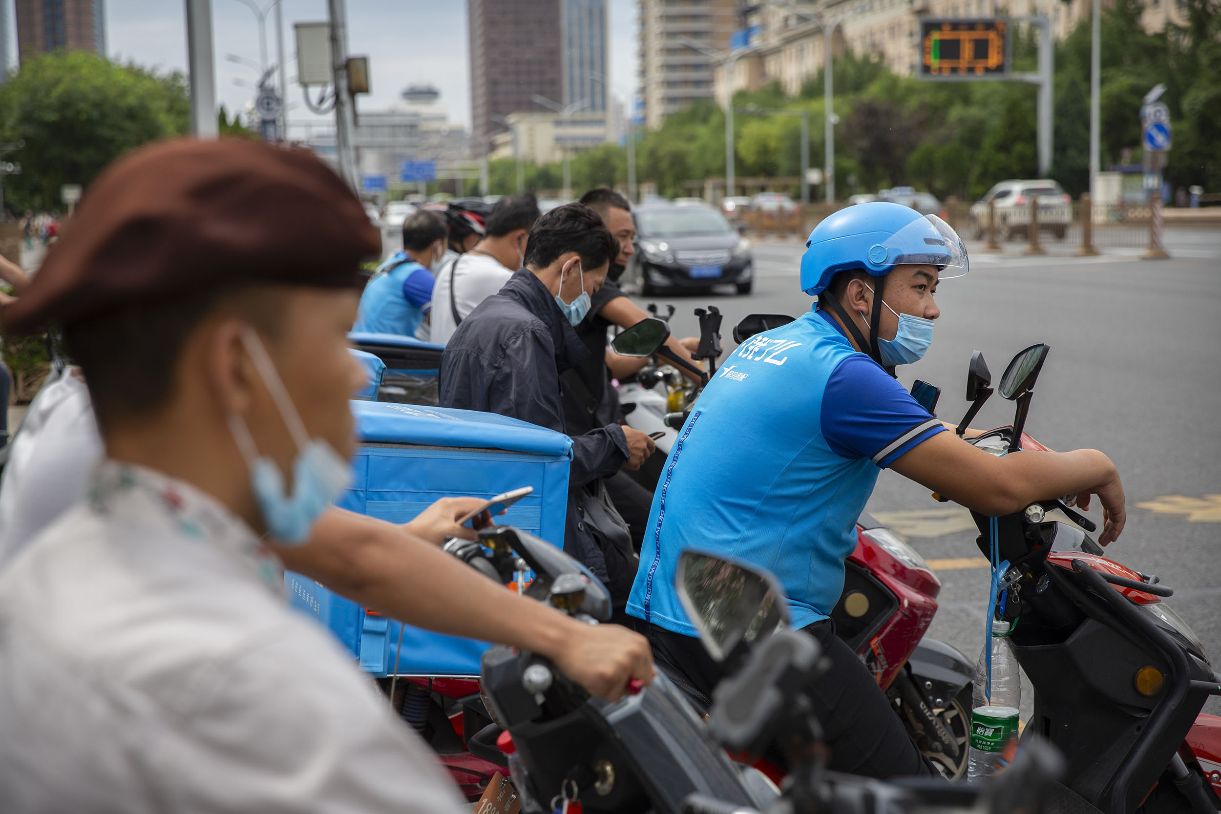 Delivery drivers wearing face masks to protect against the coronavirus wait to cross an intersection in Beijing, on Wednesday, August 19.  