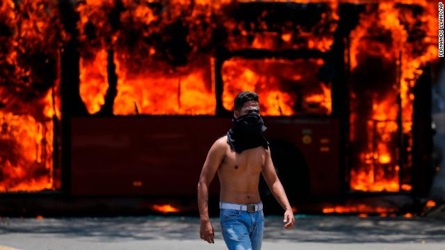 An anti-government protester walks near a bus that was set on fire by opponents of Venezuela's President Nicolás Maduro during clashes between rebel and loyalist soldiers in Caracas, Venezuela, Tuesday. 