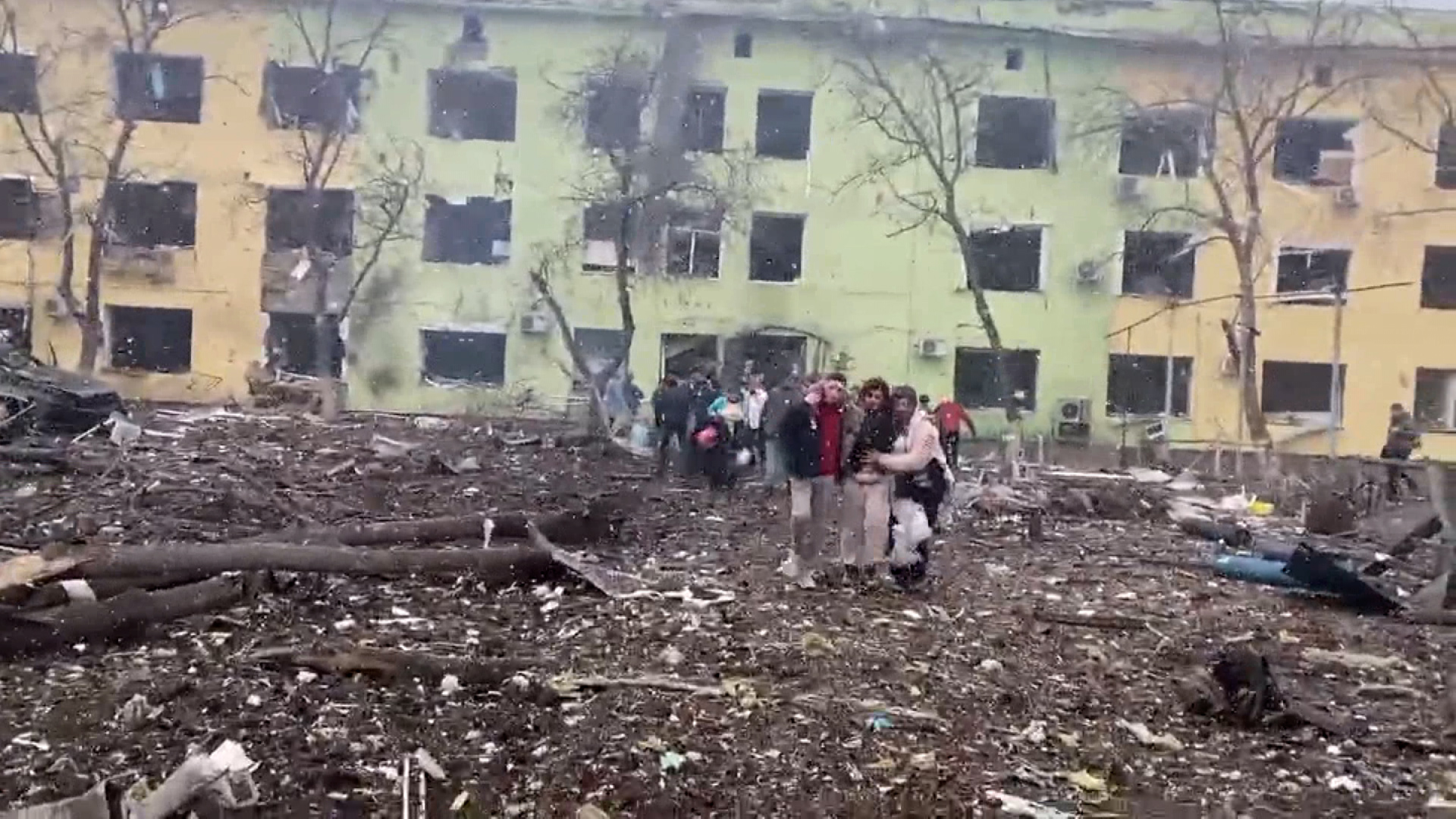 People are assisted as they leave a building at the site of a bombing at a hospital in Mariupol.
