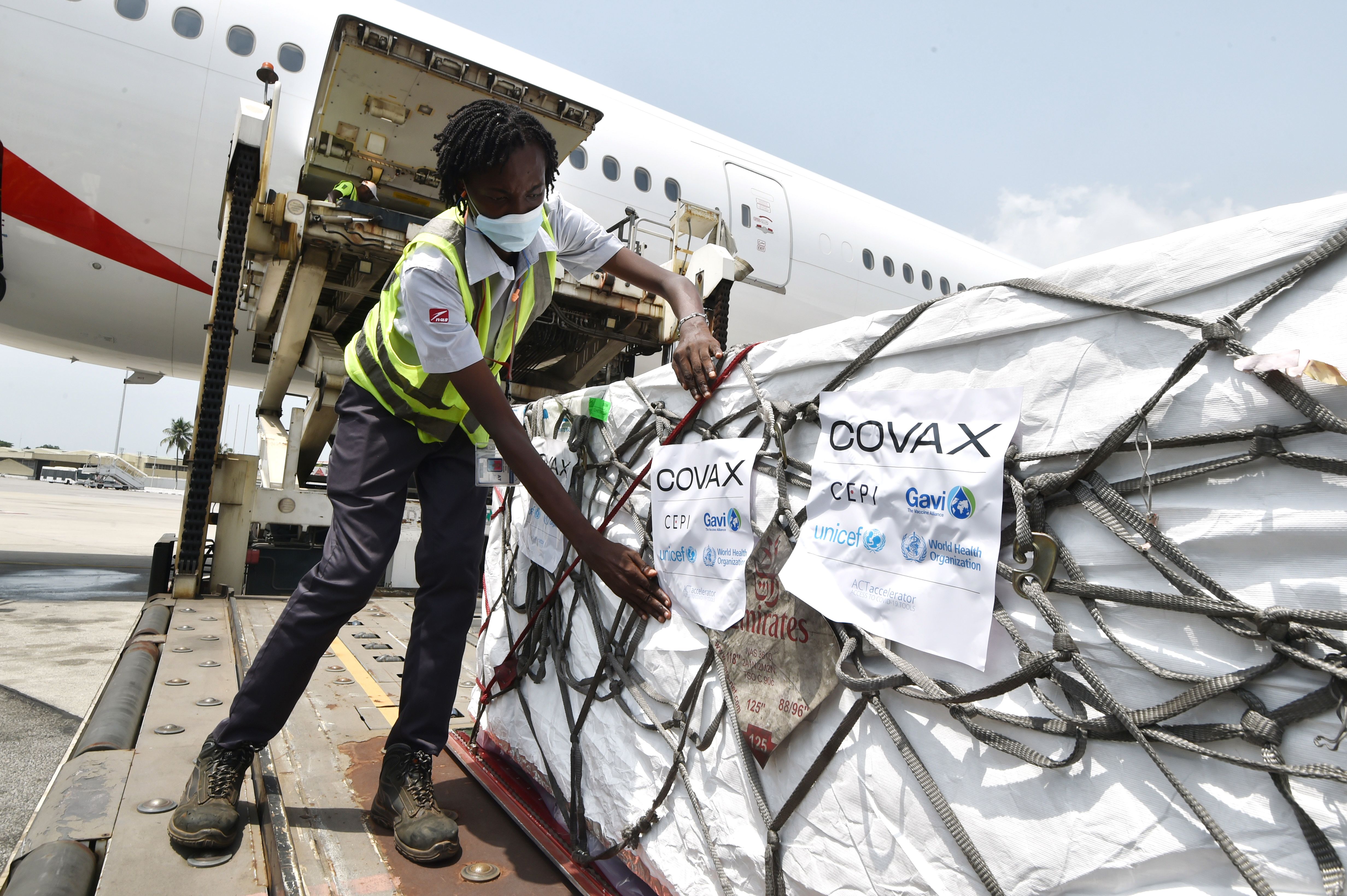 A woman puts Covax stickers as workers unload a shipment of AstraZeneca Covid-19 vaccine from a plane at Felix Houphouet Boigny airport of Abidjan on February 26, 2021. - Ivory Coast has received 504.000 doses of AstraZeneca Covid-19 vaccine on February 26. Covax is a global scheme to procure and distribute inoculations for free, as the world races to contain the pandemic.