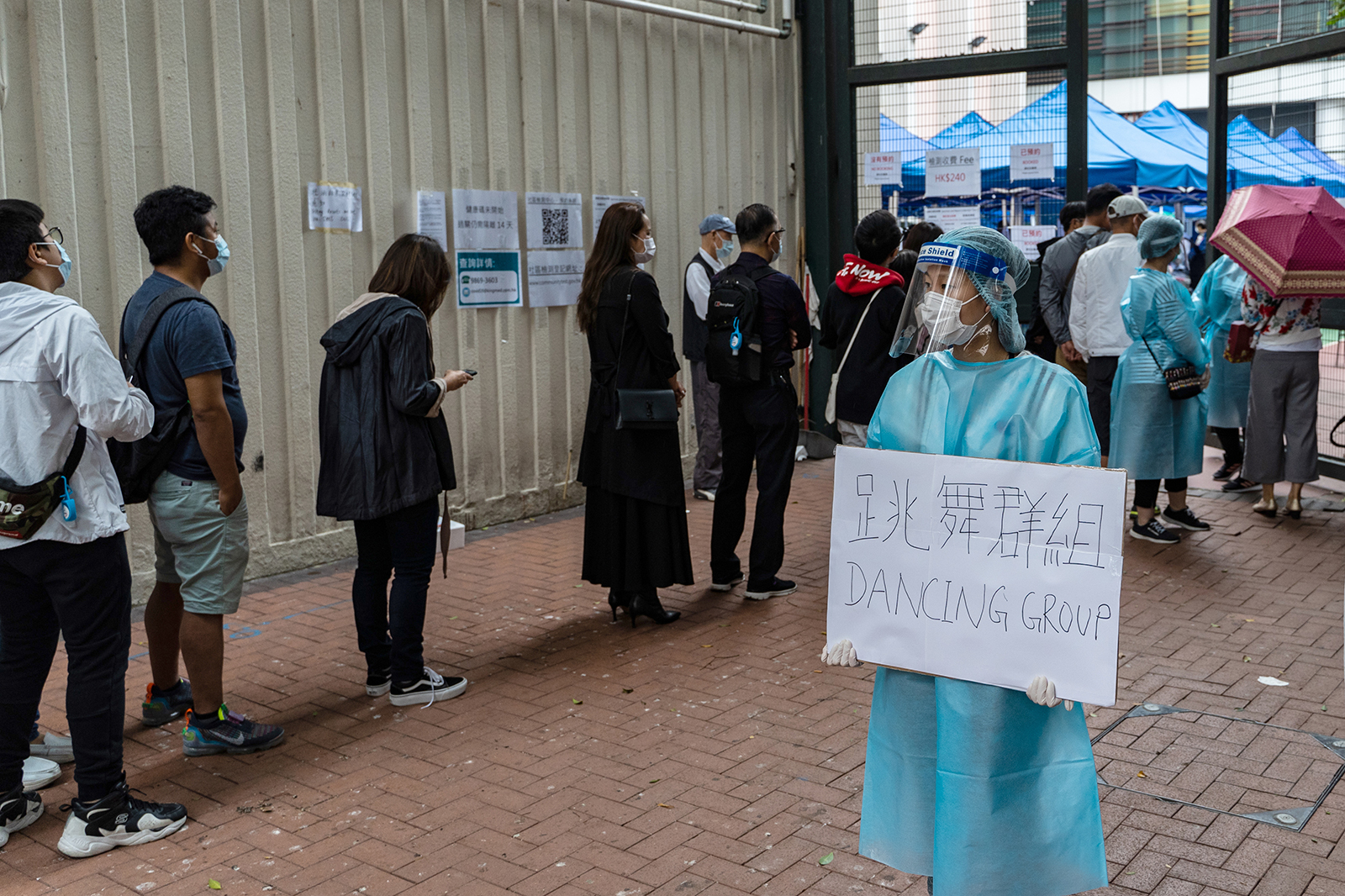 A health care worker holds a sign reading "Dancing Group," referring to a dance club cluster of Covid-19, as people stand in line outside a testing center in the Yau Ma Tei district of Hong Kong, on November. 23.