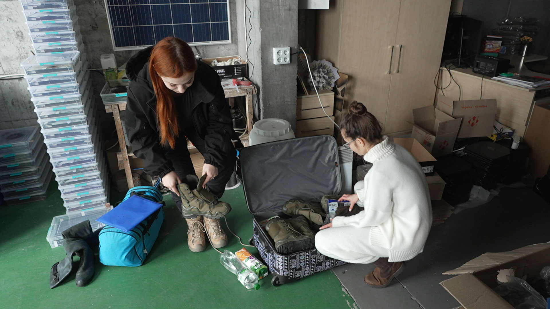 Roksolana, left, tries on her new boots while Kseniia Drahanyuk, the co-founder of the Zemlyachki NGO, helps her fill a suitcase with various items.