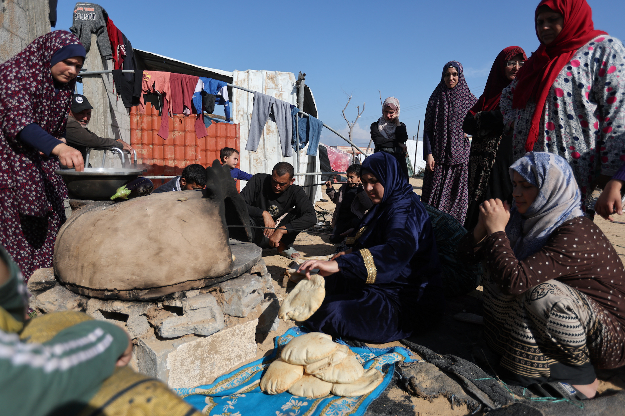 People wait while a woman prepares food in southern Gaza on Wednesday.