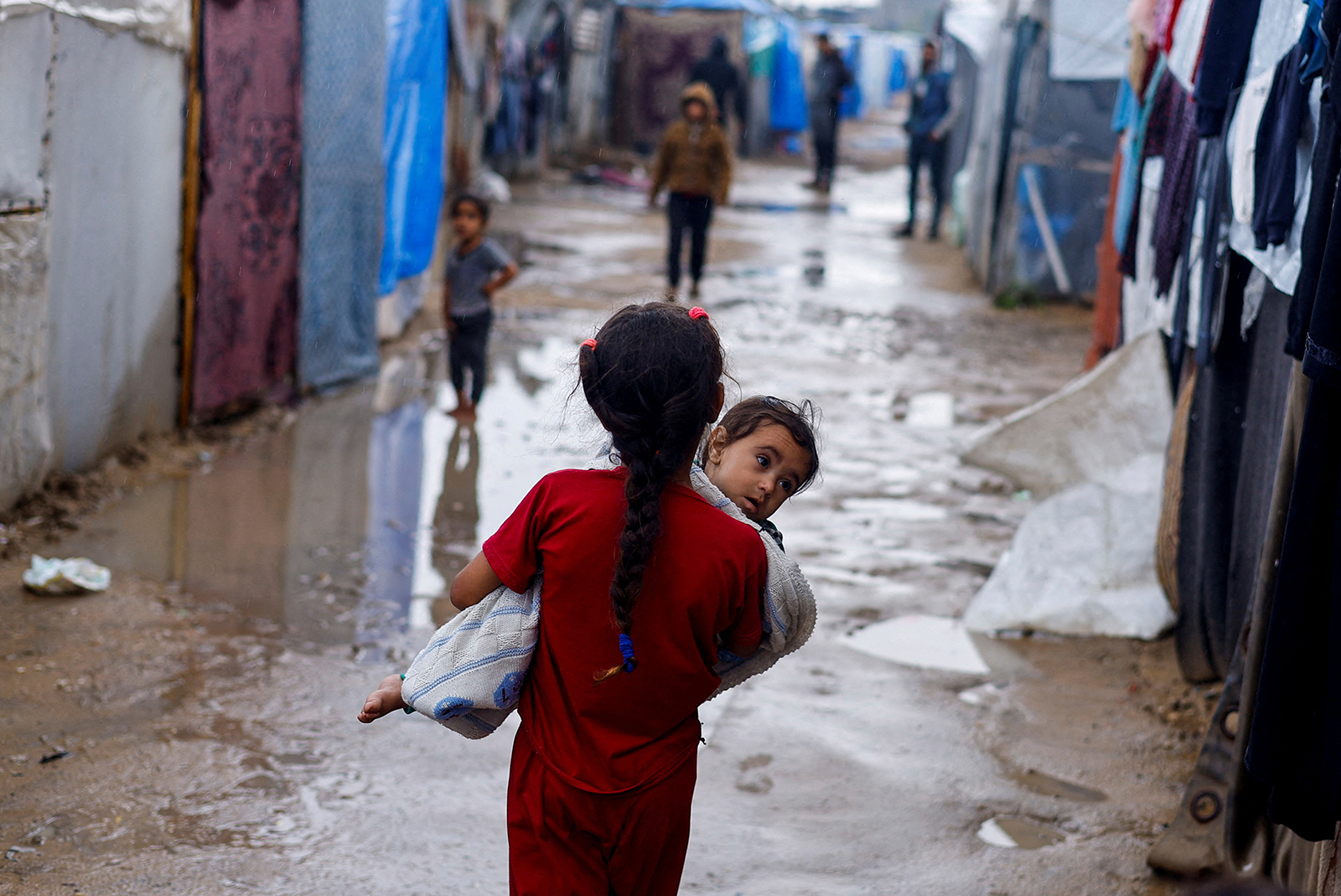 A displaced Palestinian girl holds a child as she walks at a tent camp on a rainy day in Rafah, Gaza on May 6.