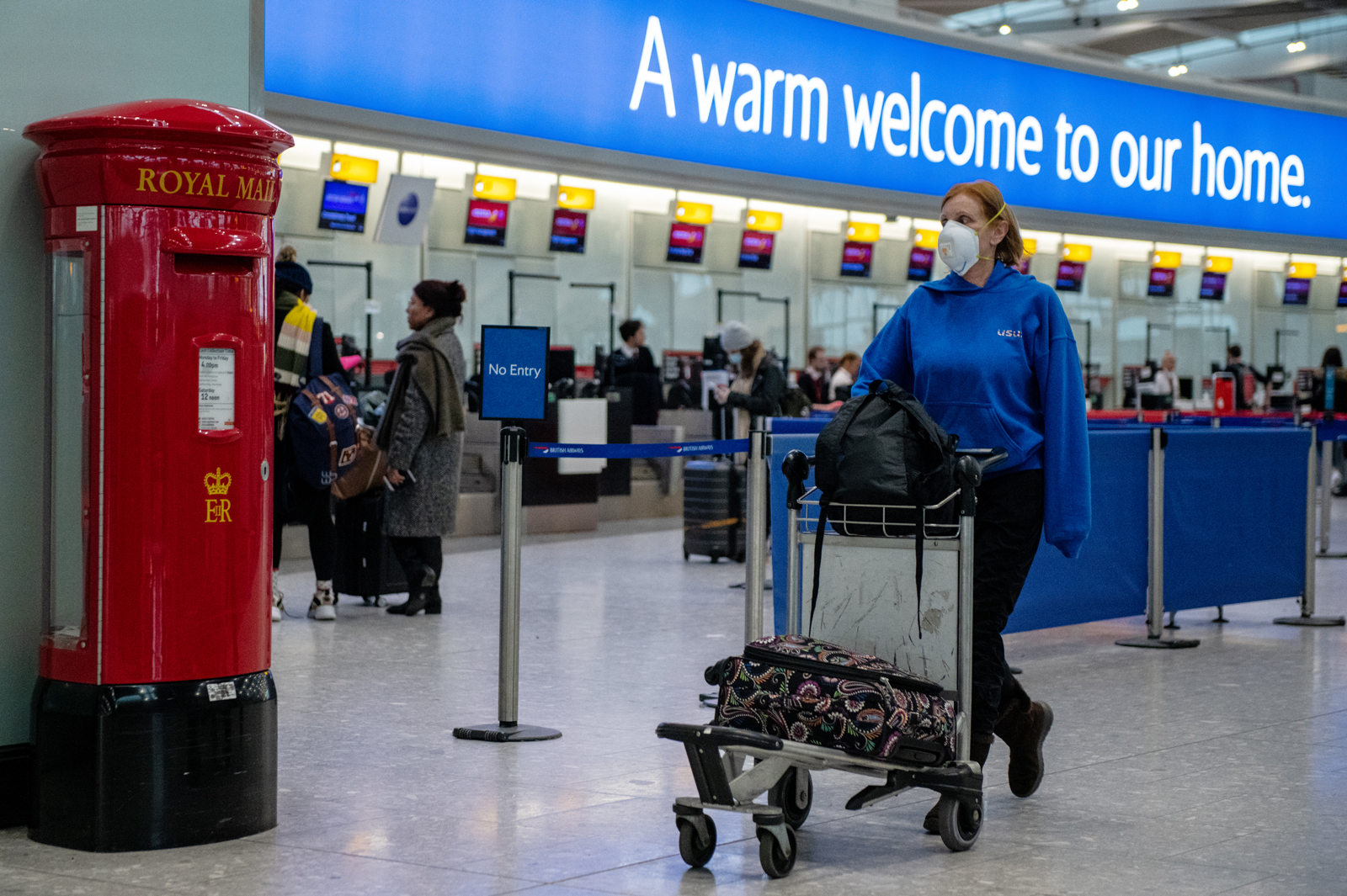 An airline passenger wearing a face mask pushes her bags past a post box at Heathrow Terminal 5 departures on March 15, in London.