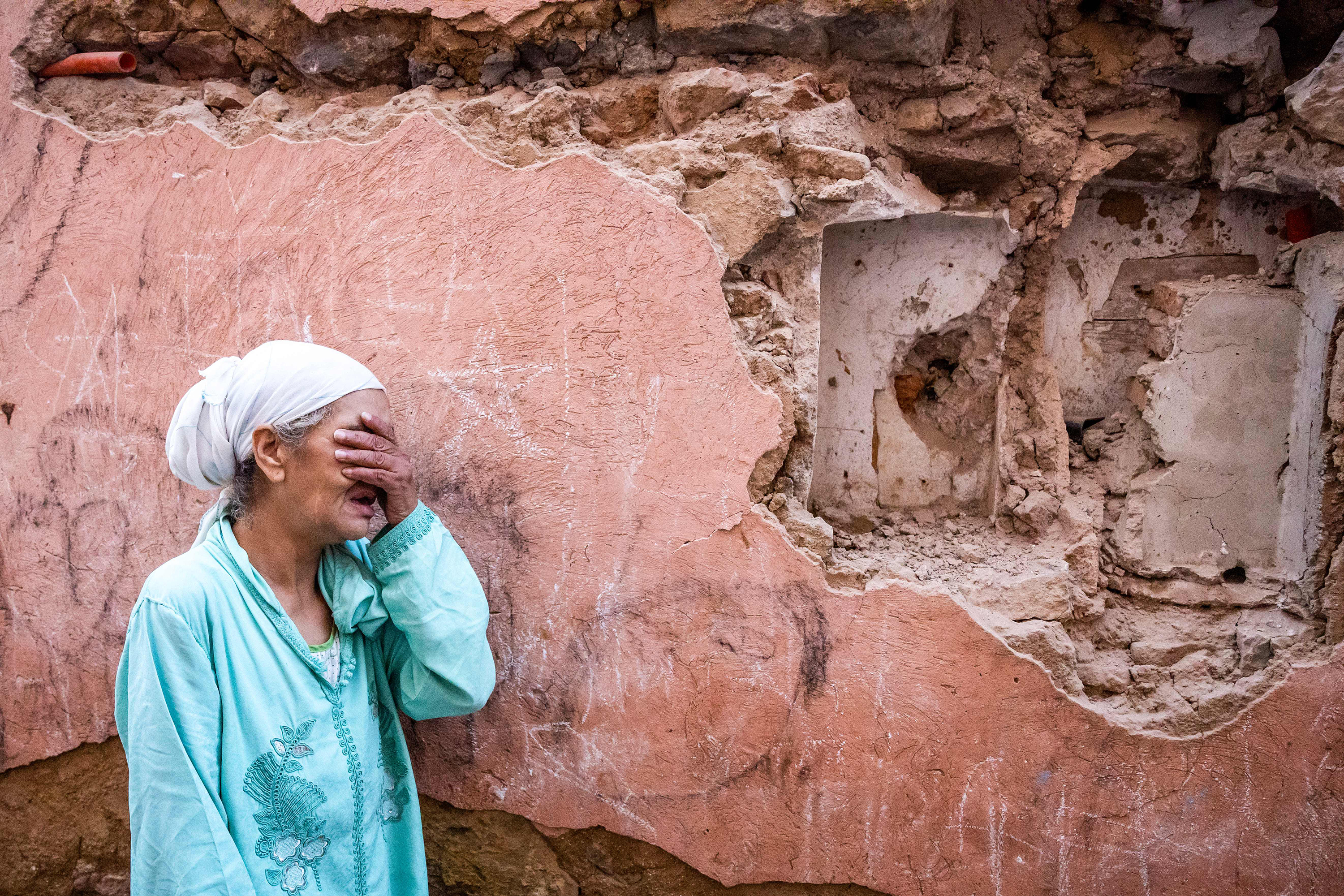 A woman reacts standing in front of her earthquake-damaged house.