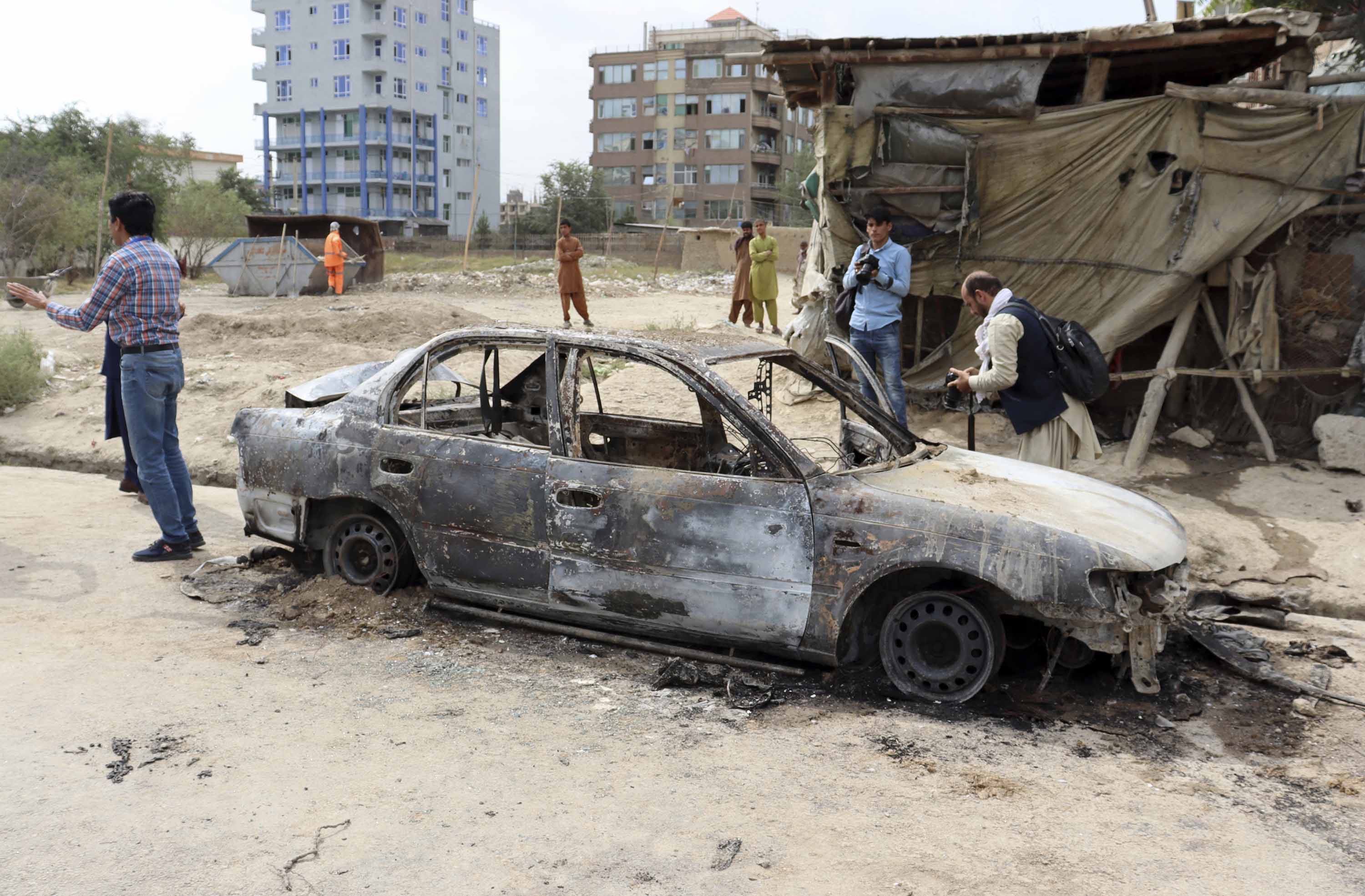 Journalists take photos of a destroyed vehicle where rockets were fired from, in Kabul, Afghanistan, on Monday, August 30. 