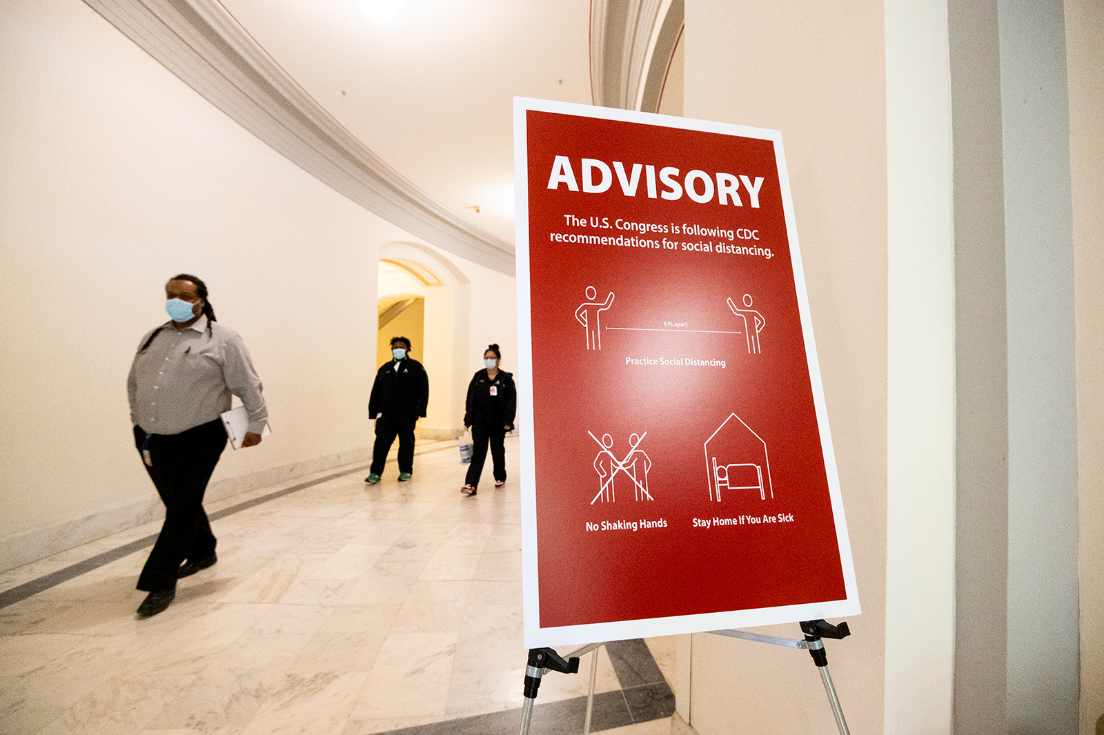 Capitol workers wearing face masks walk past a sign advising people to observe social distancing in the Russell Senate Office Building on Monday, May 4.