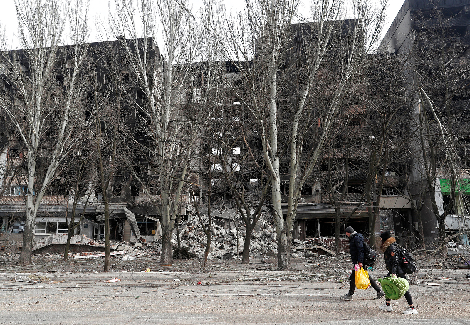 Local residents walk past a destroyed apartment building in the besieged southern port city of Mariupol, Ukraine, on March 31.