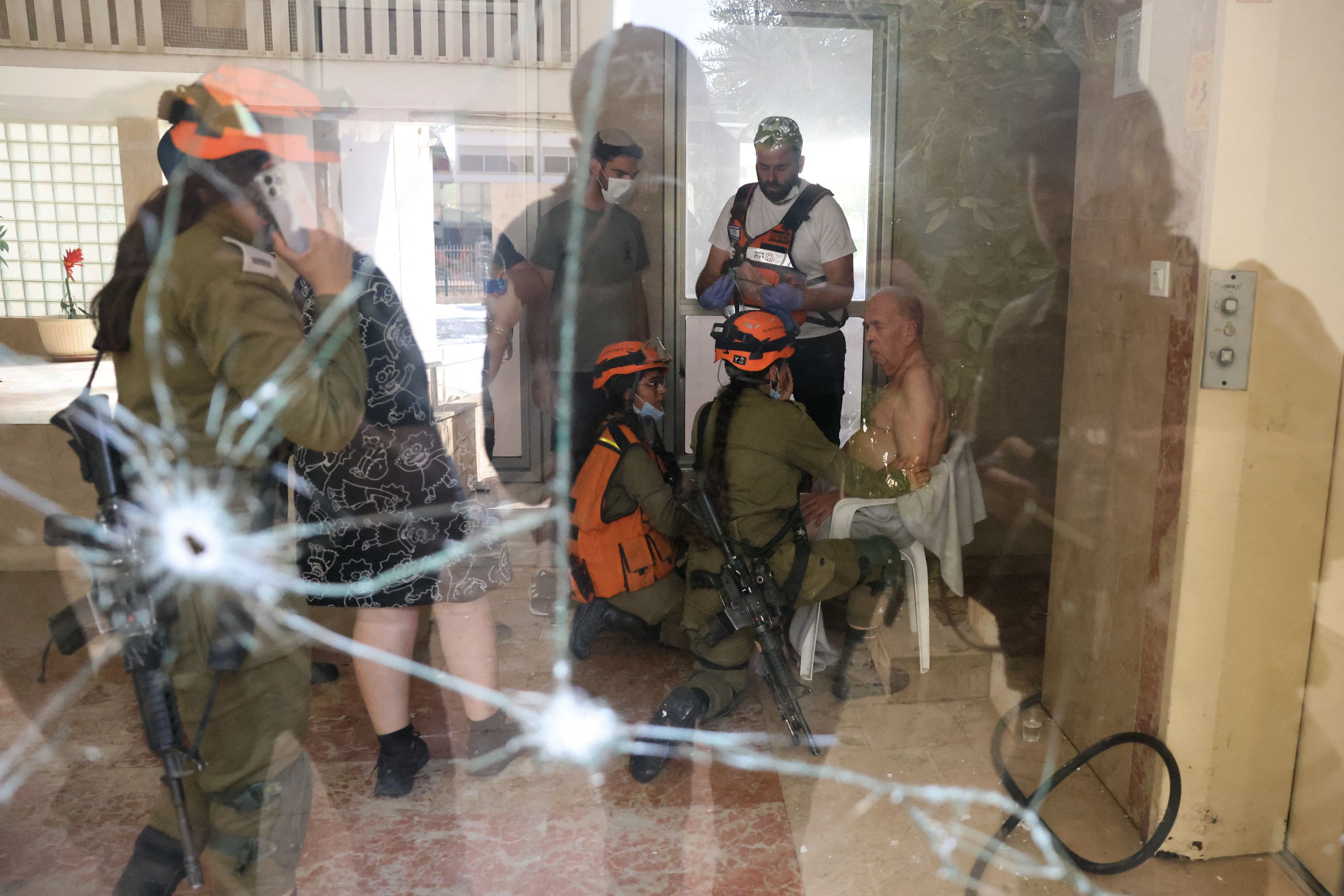 Israeli rescue teams tend to an elderly man seated on a chair in the entrance of a building that received a direct hit in Ashkelon during a rocket attack from the Gaza Strip in southern Israel, on October 7, 2023.