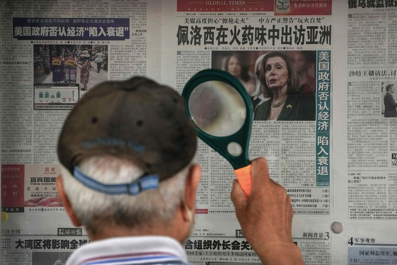 A man uses a magnifying glass to read a newspaper headline reporting on US House Speaker Nancy Pelosi's Asia visit at a stand in Beijing on Sunday, July 31.