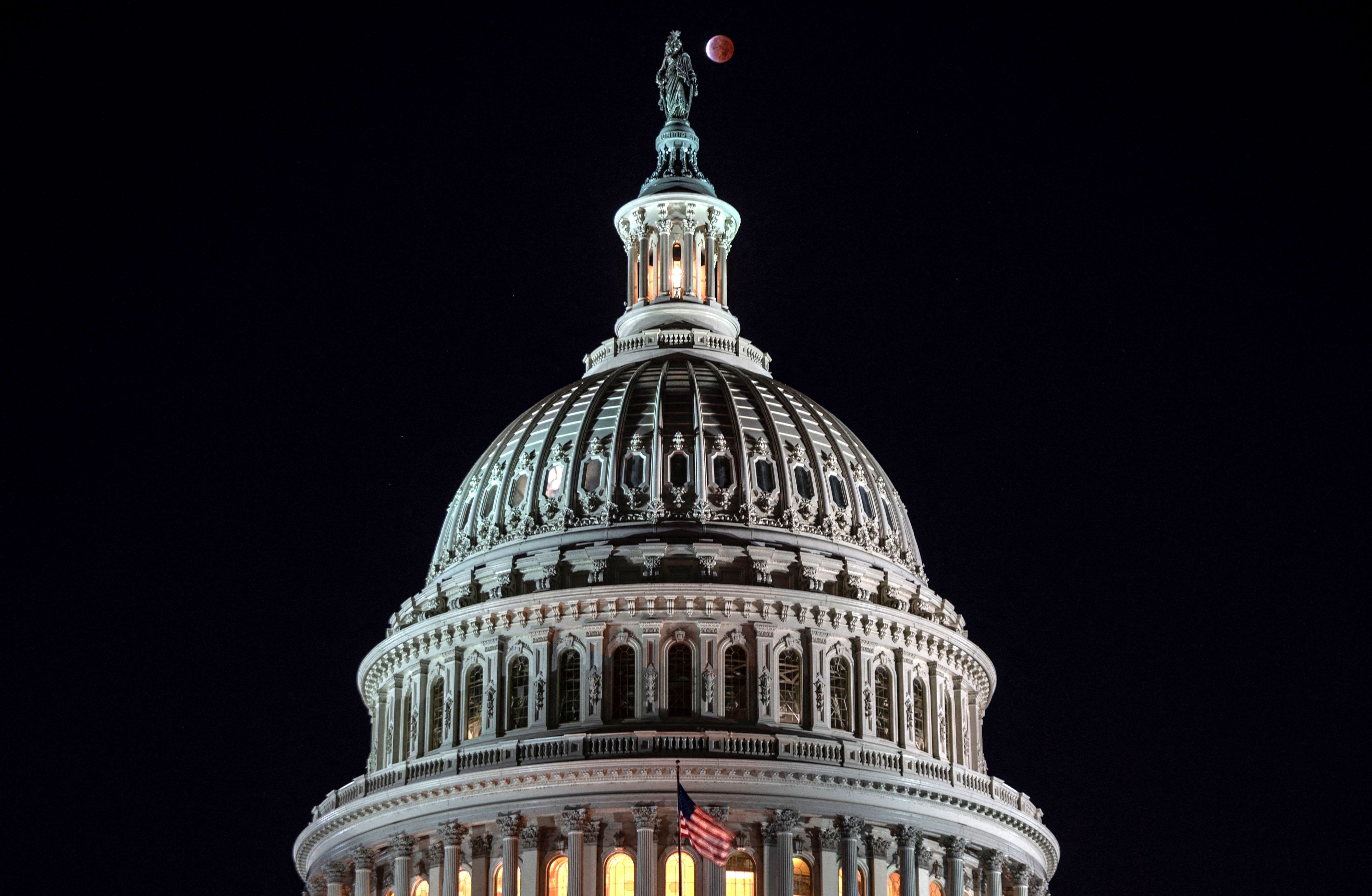 The moon, with a partial lunar eclipse, is seen behind the dome of the Capitol in Washington, DC, early on November 19.