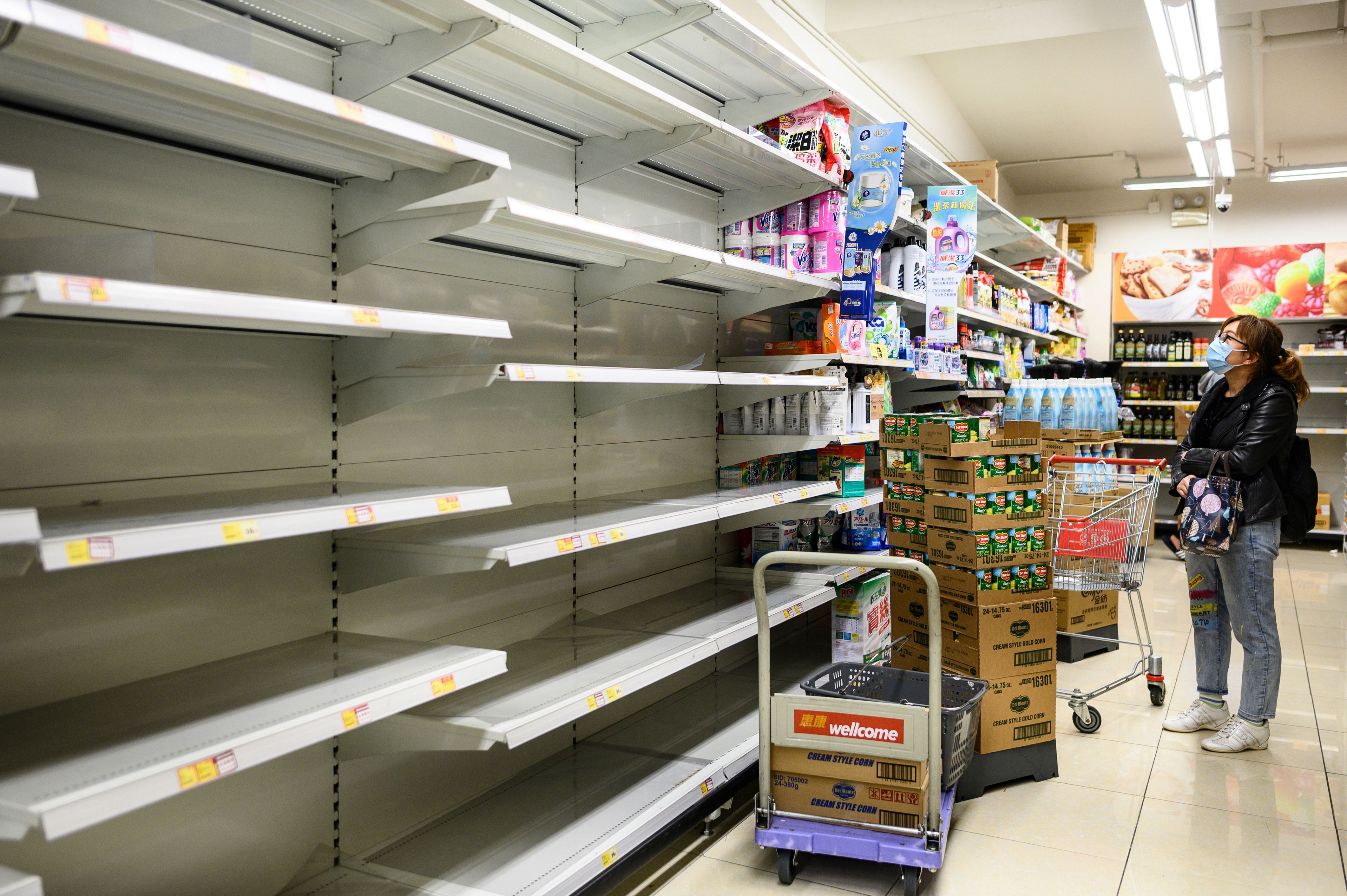 A woman looks at empty supermarket shelves, usually used for stacking paper towels, in Hong Kong on February 5, 2020.