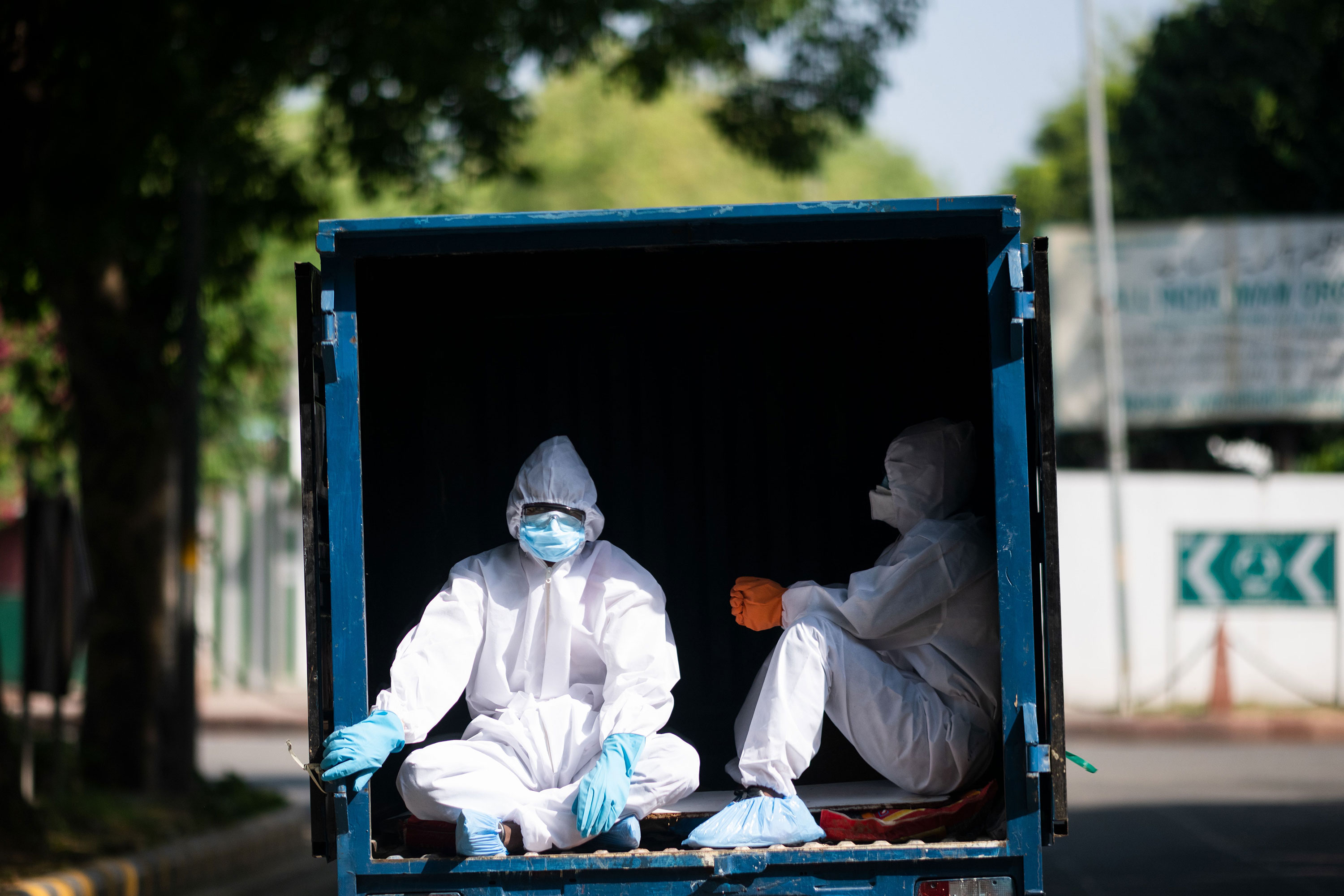 Men wearing protective clothing ride in the back of a vehicle in New Delhi on May 4.