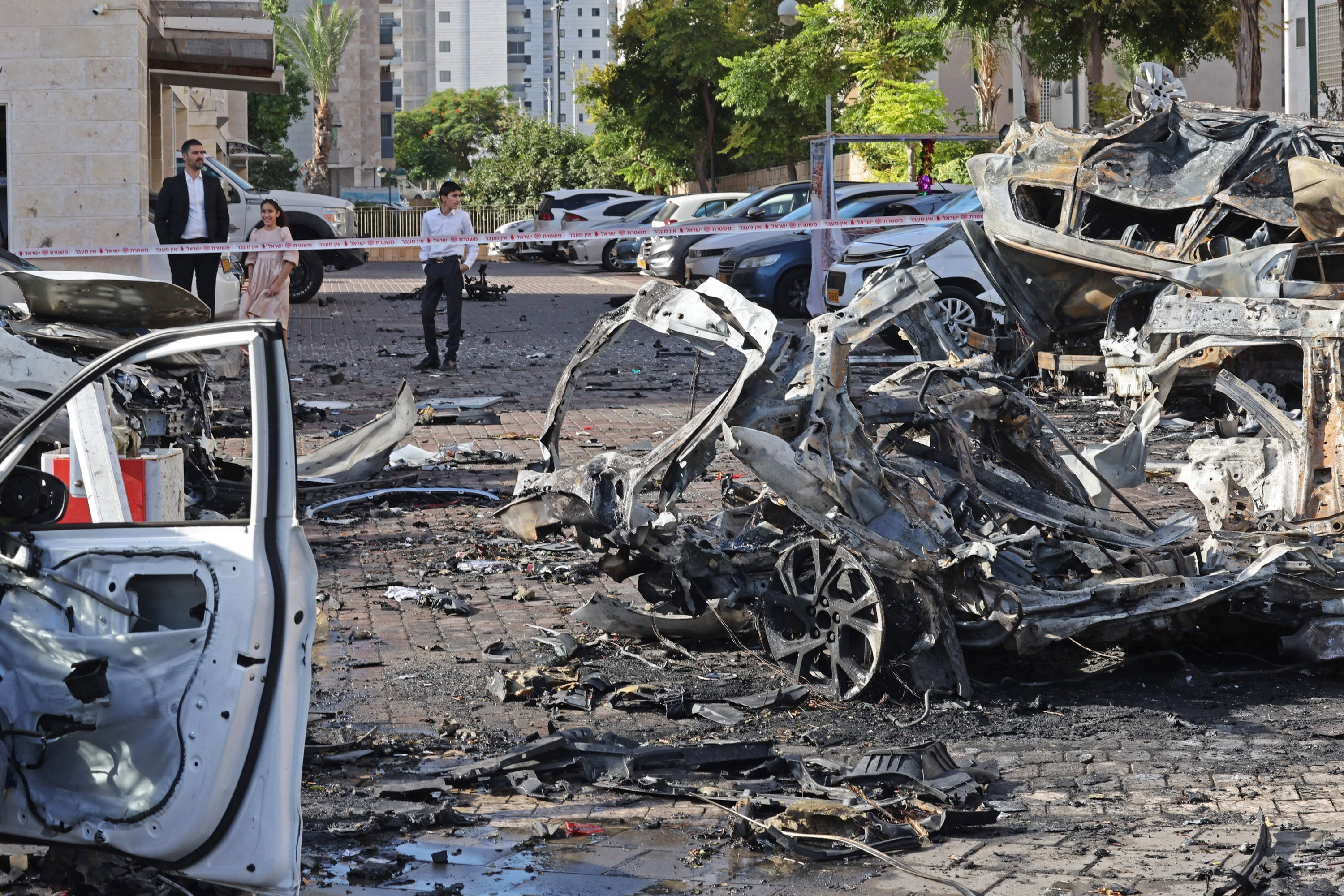 Residents look at the wreckage of destroyed vehicles in Ashkelon following a rocket attack from the Gaza Strip into southern Israel on October 7, 2023.