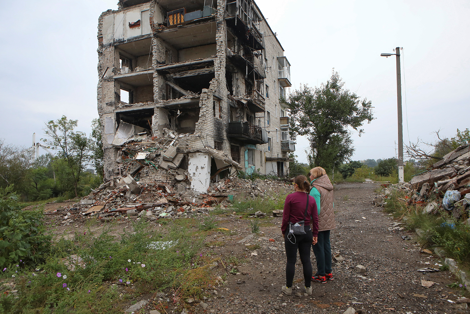 Women stand near a residential building destroyed by a military strike in the town of Izium recently liberated by the Ukrainian Armed Forces on September 15.