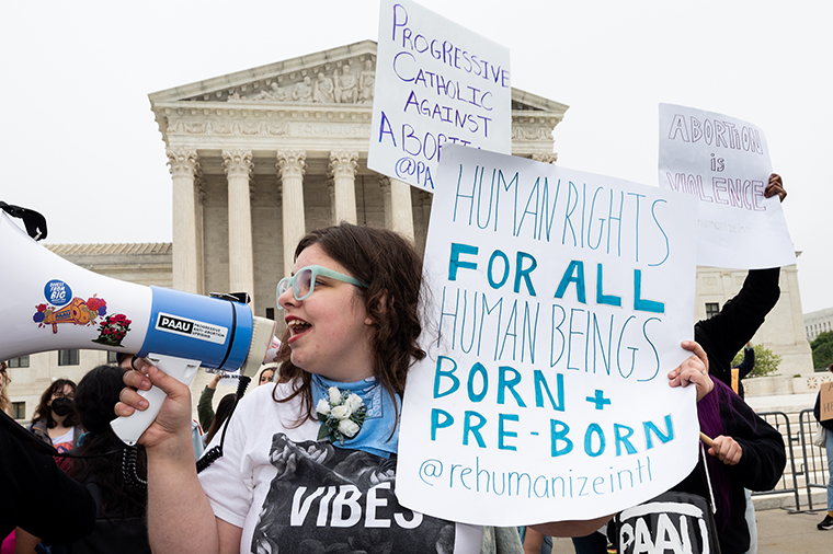 A woman holds a sign saying "Human rights for all human beings born + pre-born."