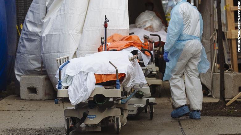 A medical worker in protective clothing walks past the bodies of deceased patients from a refrigerated overflow morgue outside the Wyckoff Heights Medical Center in Brooklyn, New York, on Friday, April 3. 