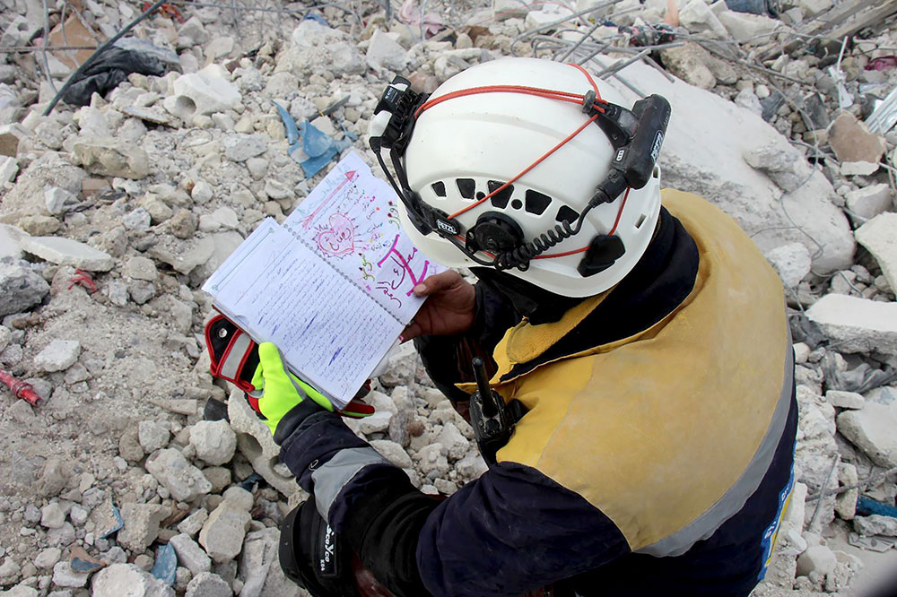 A member of the White Helmets looks through a notebook found in the rubble.