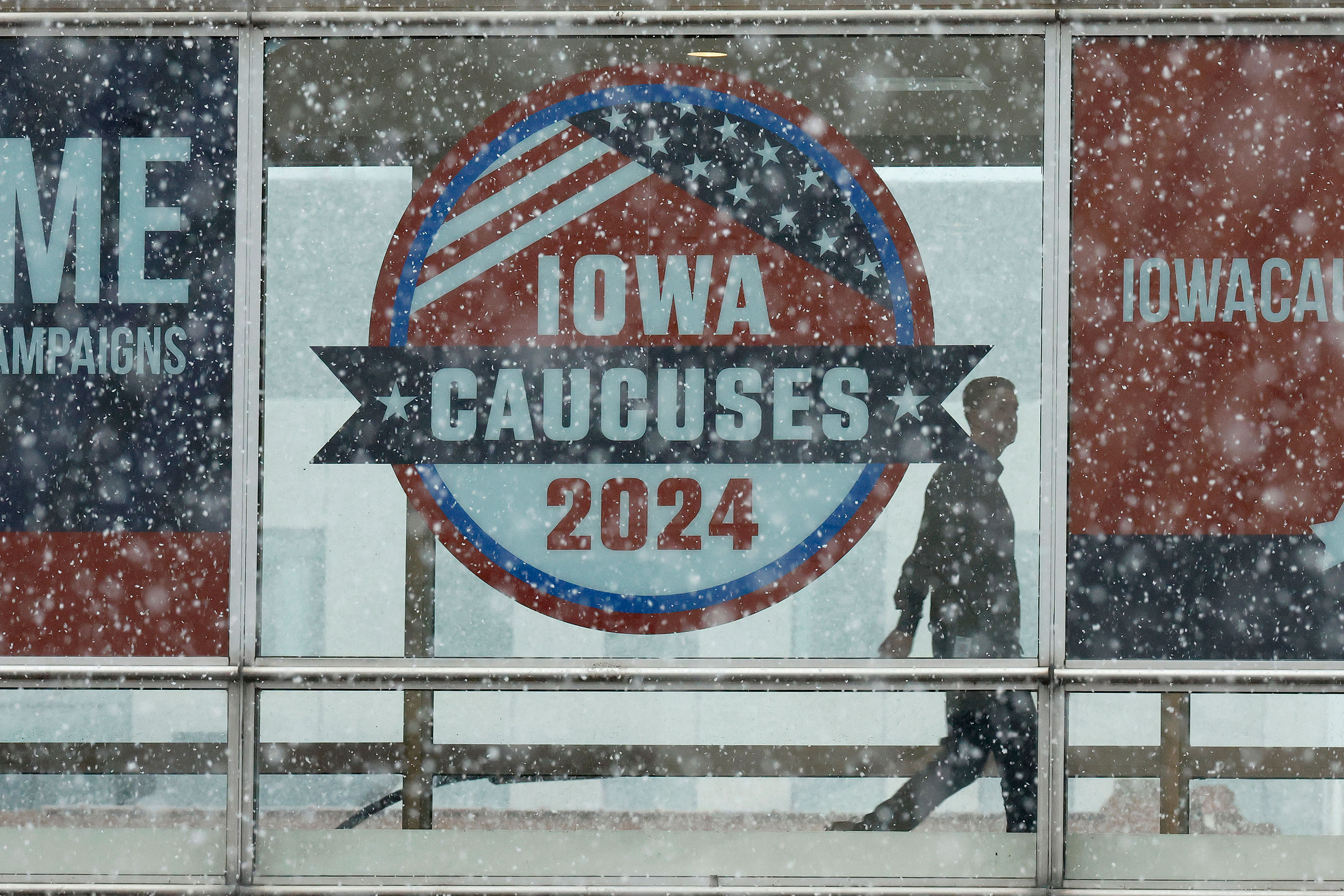 Snow falls as a man walks past caucus signs in downtown Des Moines, Iowa, on Monday.