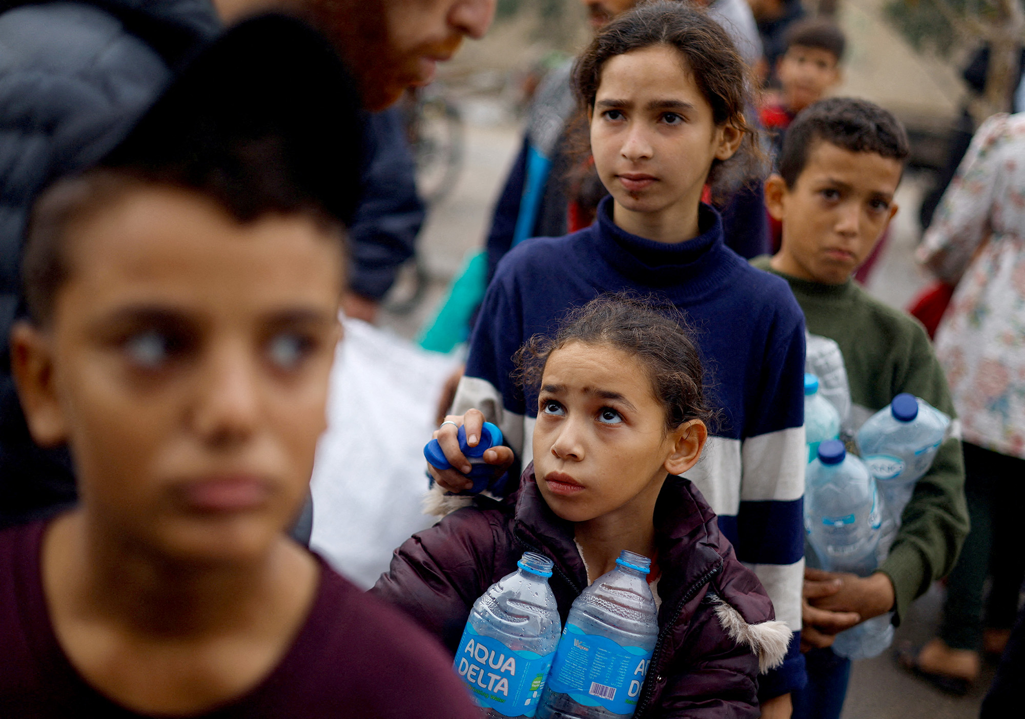 Palestinian children hold empty water bottles as they queue to collect water in Rafah, Gaza, on December 5.