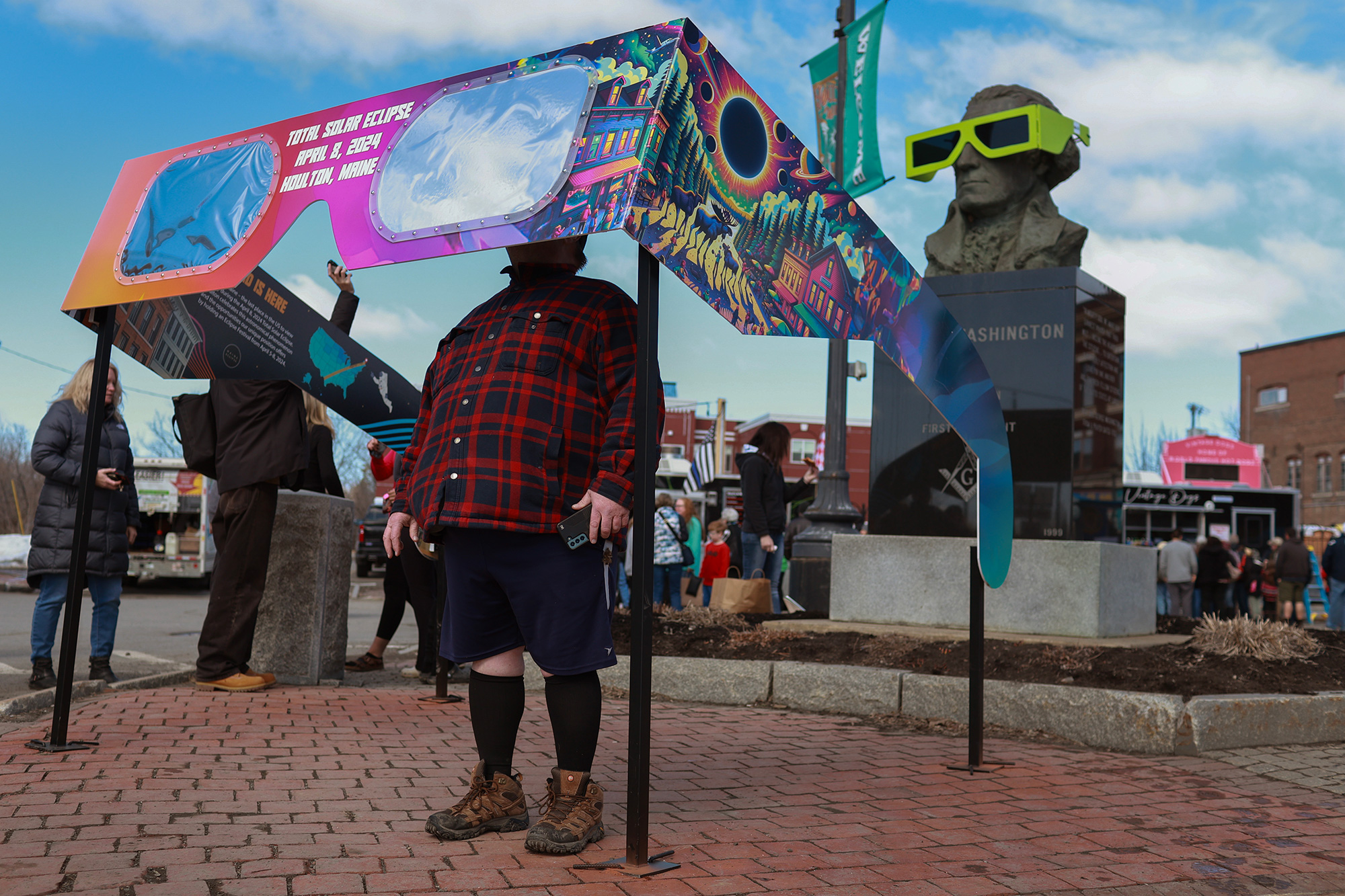 Visitors look through a pair of oversized eclipse glasses set up in the town square in Houlton, Maine, on Sunday.