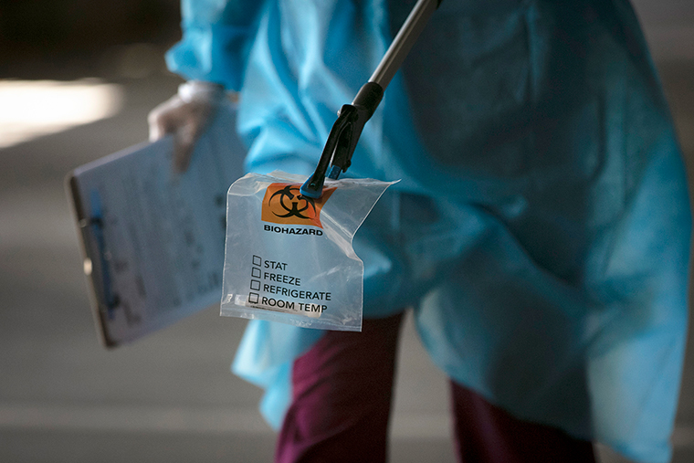 A physician assistant carries a nasal swab sample using a grabber at a drive-through testing site set up at the Anaheim Convention Center in Anaheim, California, on Thursday, July 16.