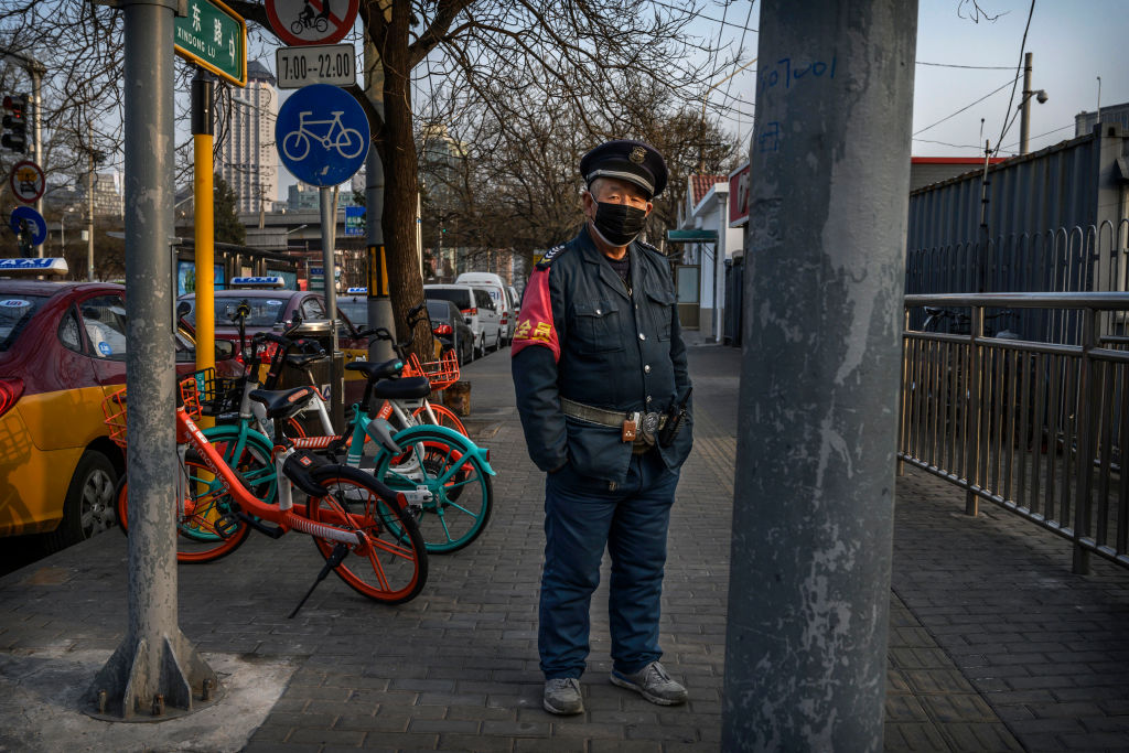 2020年2月25日，一名中国过境工人在中国北京的一个公交车站等车时戴着防护口罩。 