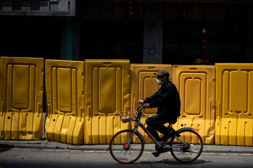 A face mask-clad cyclist rides alongside a barricade separating a residential compound in Wuhan, in China's central Hubei province, on April 6, after some restrictions amid the coronavirus pandemic were eased in the city. 