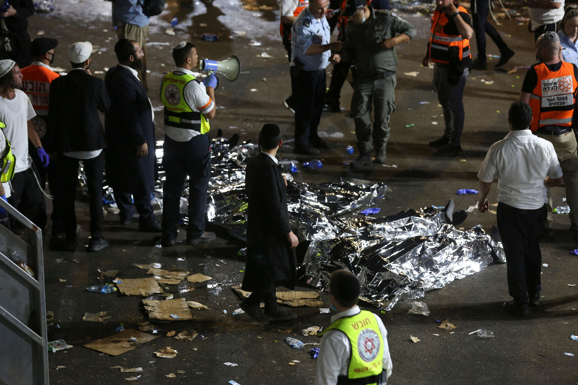 Ultra-Orthodox Jewish men stand next to covered bodies after dozens of people were killed and others injured during Lag Ba'omer celebrations at Mount Meron on April 30.