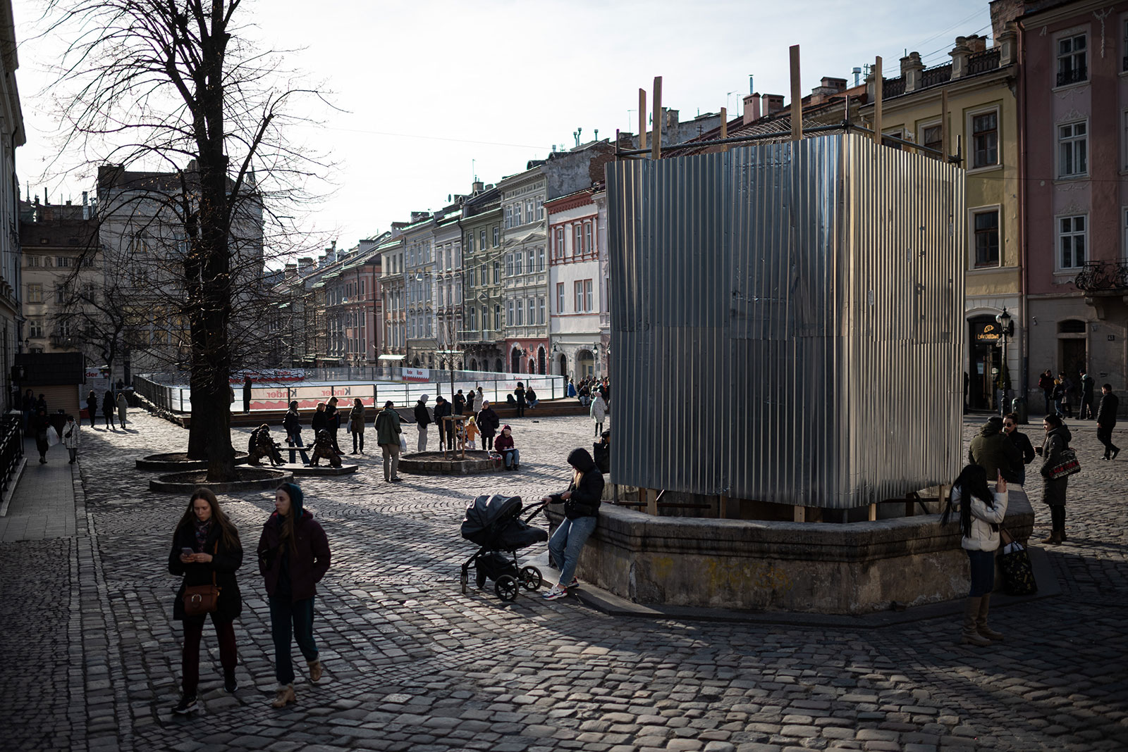 People walk by a monument covered by protective screen in case of shelling on Sunday in Lviv. 