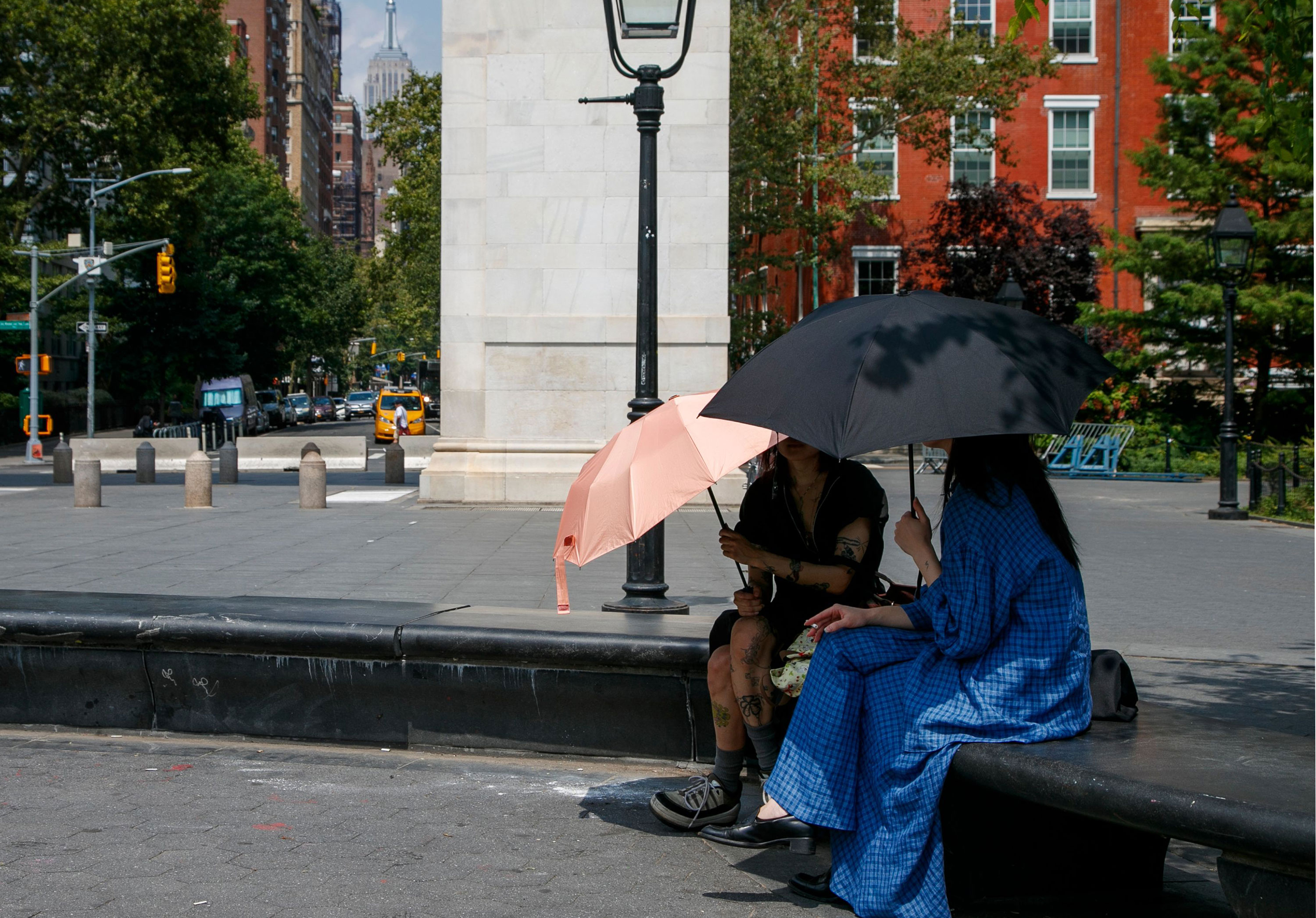 People sit with umbrellas in Washington Square Park in New York on July 27, 2023. 