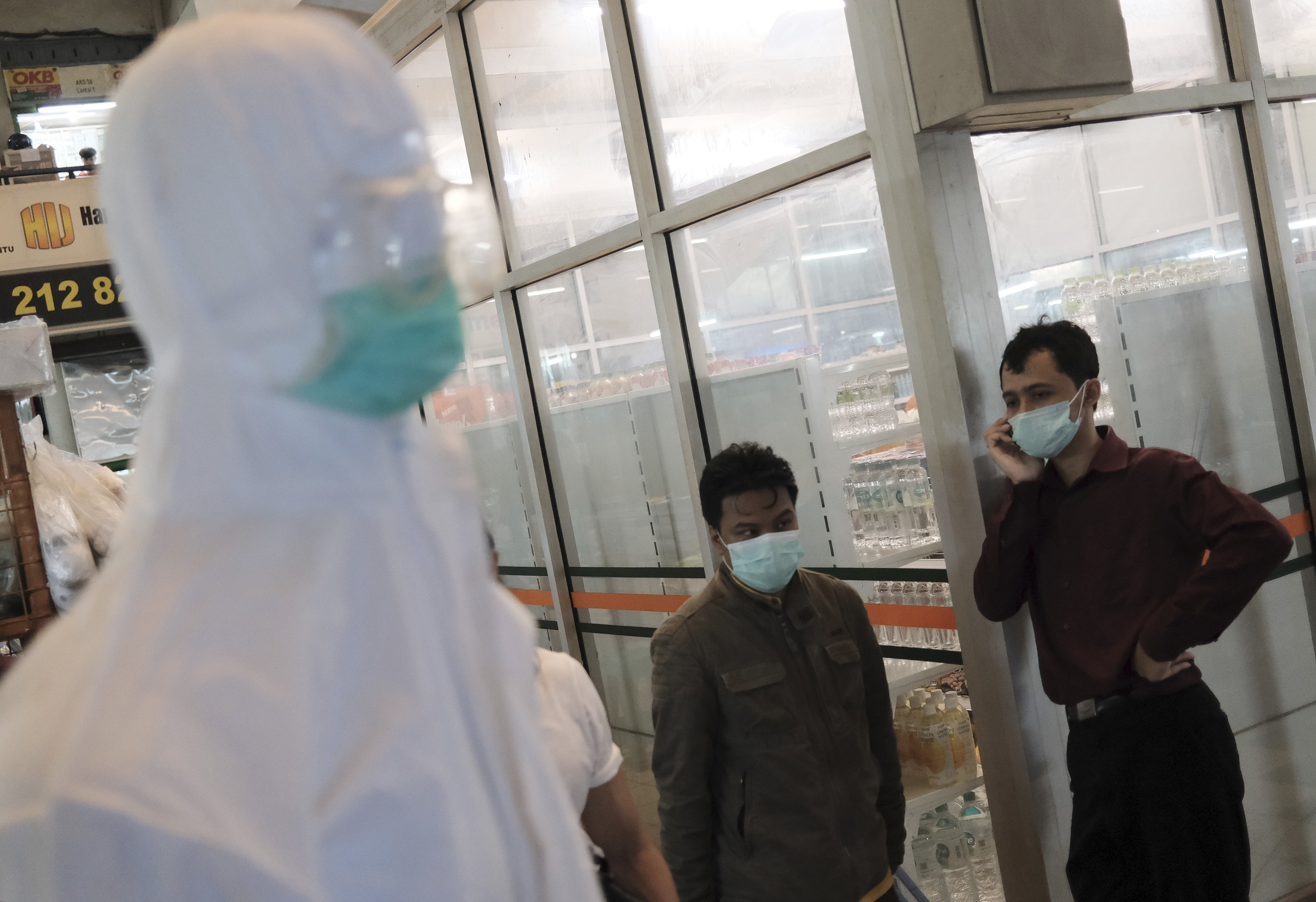 Men wearing face masks stand next to a mannequin in protective suit displayed at a shop that sells medical supplies at market in Jakarta, Indonesia, on Wednesday, March 4.