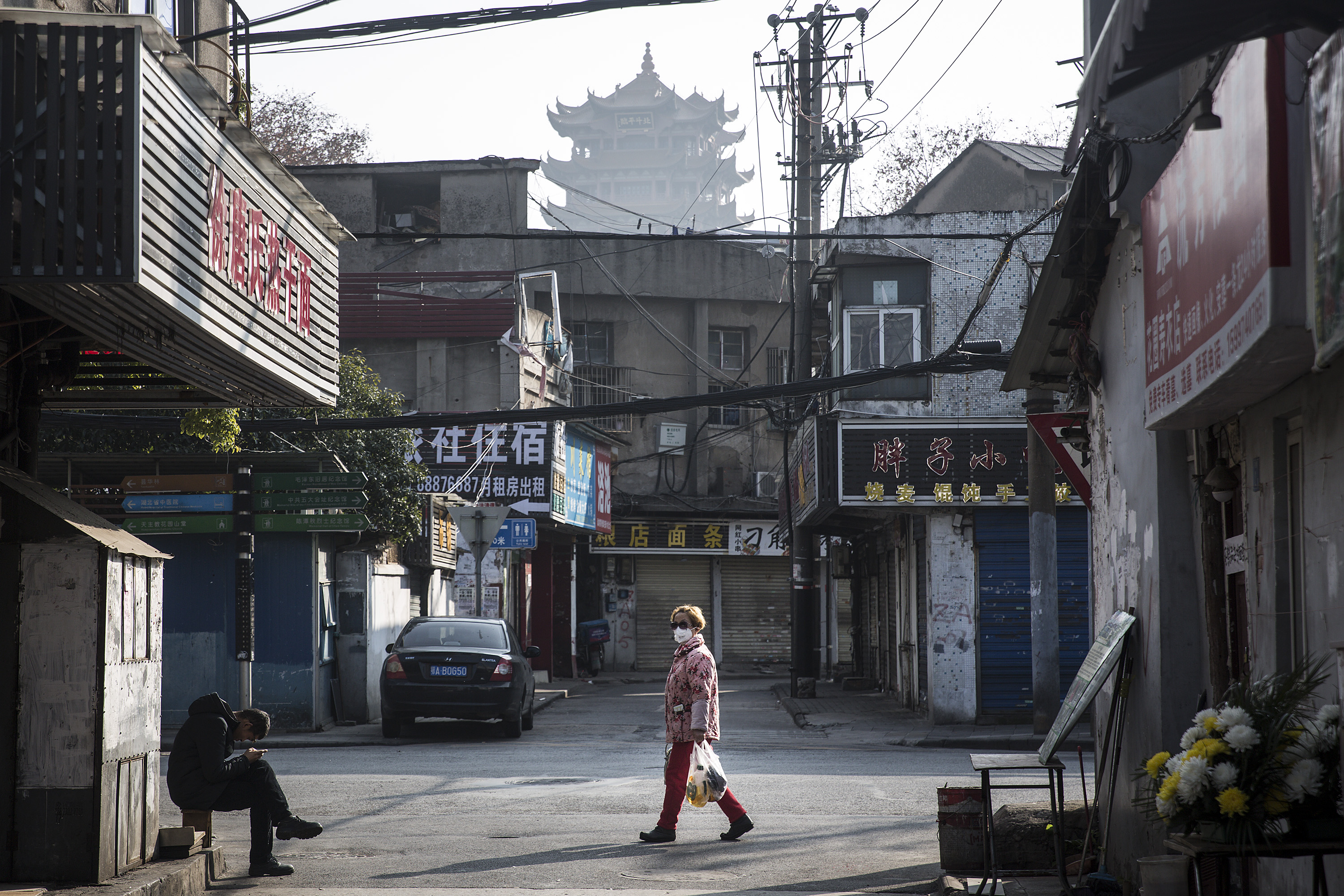  A woman wears a face mask as a man sits by the roadside on Friday in Wuhan, China.