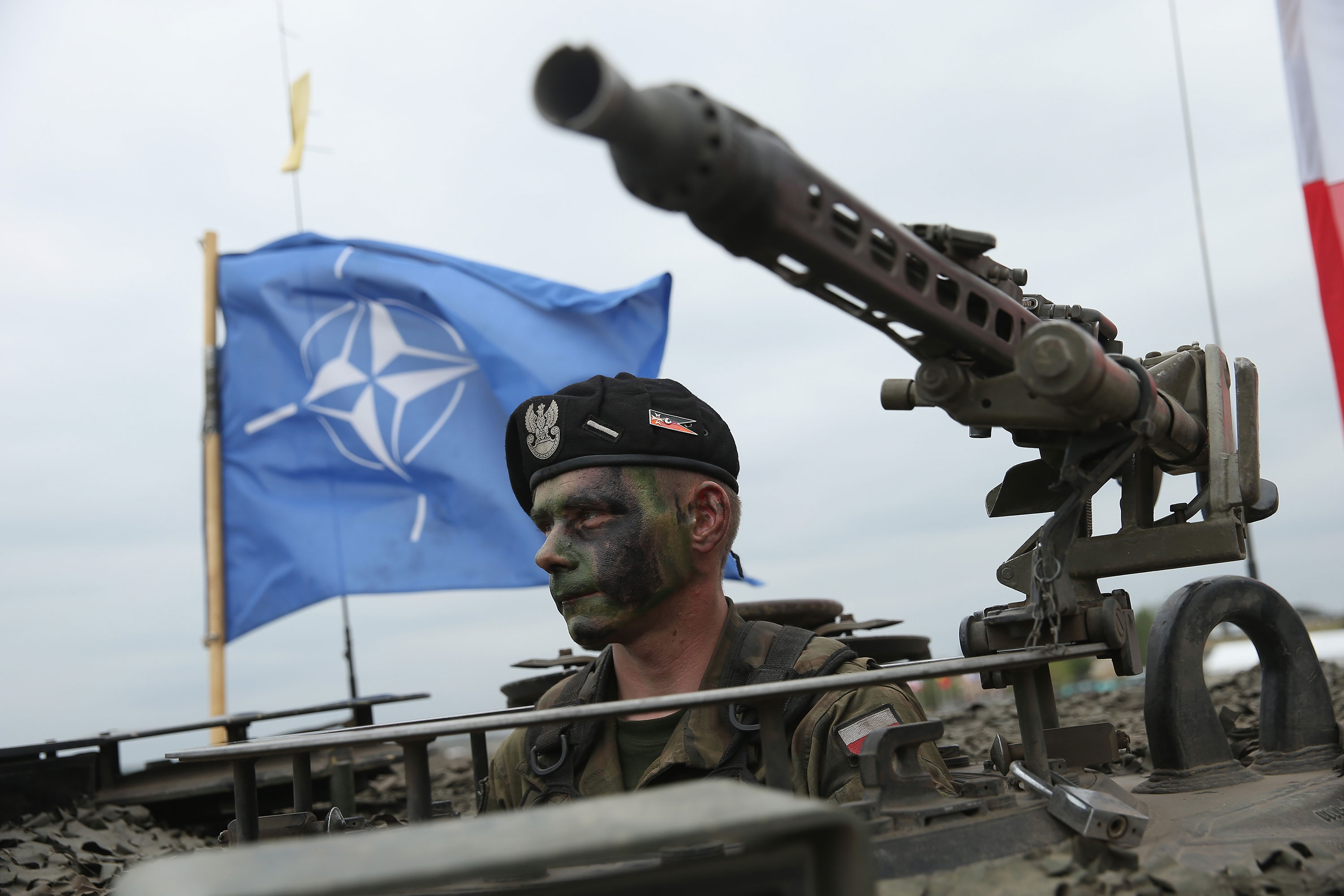 جندي مع الجيش البولندي يجلس في دبابة بينما يرفرف علم الناتو خلفه خلال مناورات عسكرية في عام 2015 في زاغان ، بولندا.