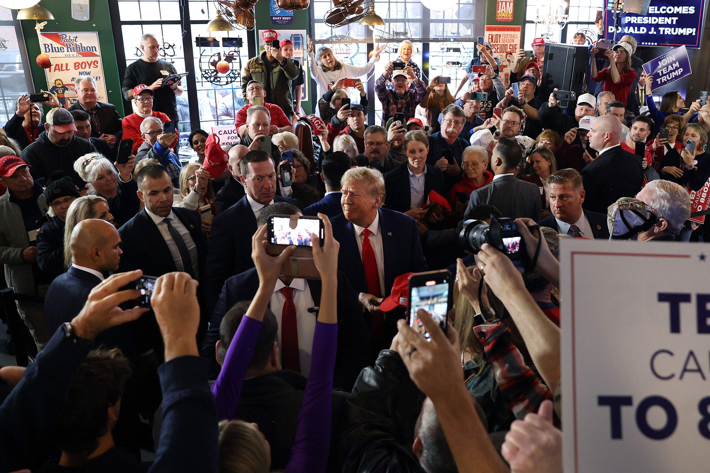 Former President Donald Trump greets guests as he arrives at a commit to caucus campaign event at the Whiskey River bar on December 2, in Ankeny, Iowa.