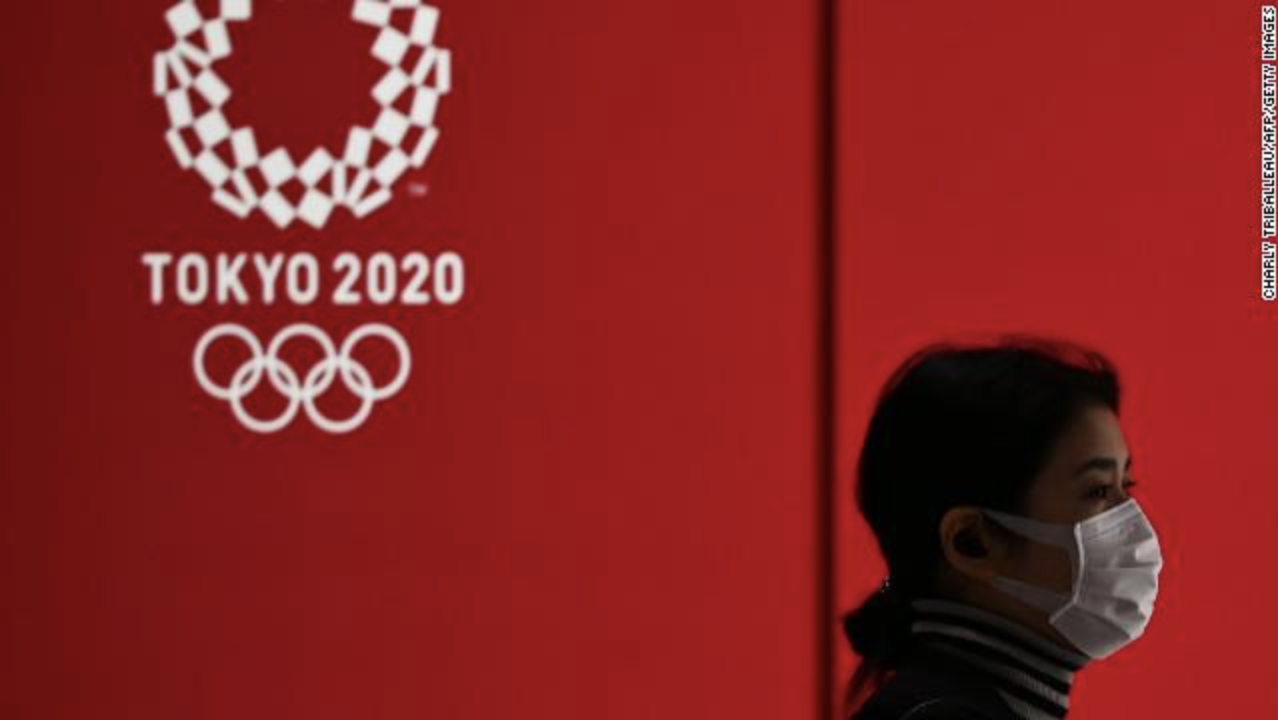 A woman in a face mask walks past a display showing the Tokyo 2020 Olympic Games logo in Tokyo on March 24, 2020. 