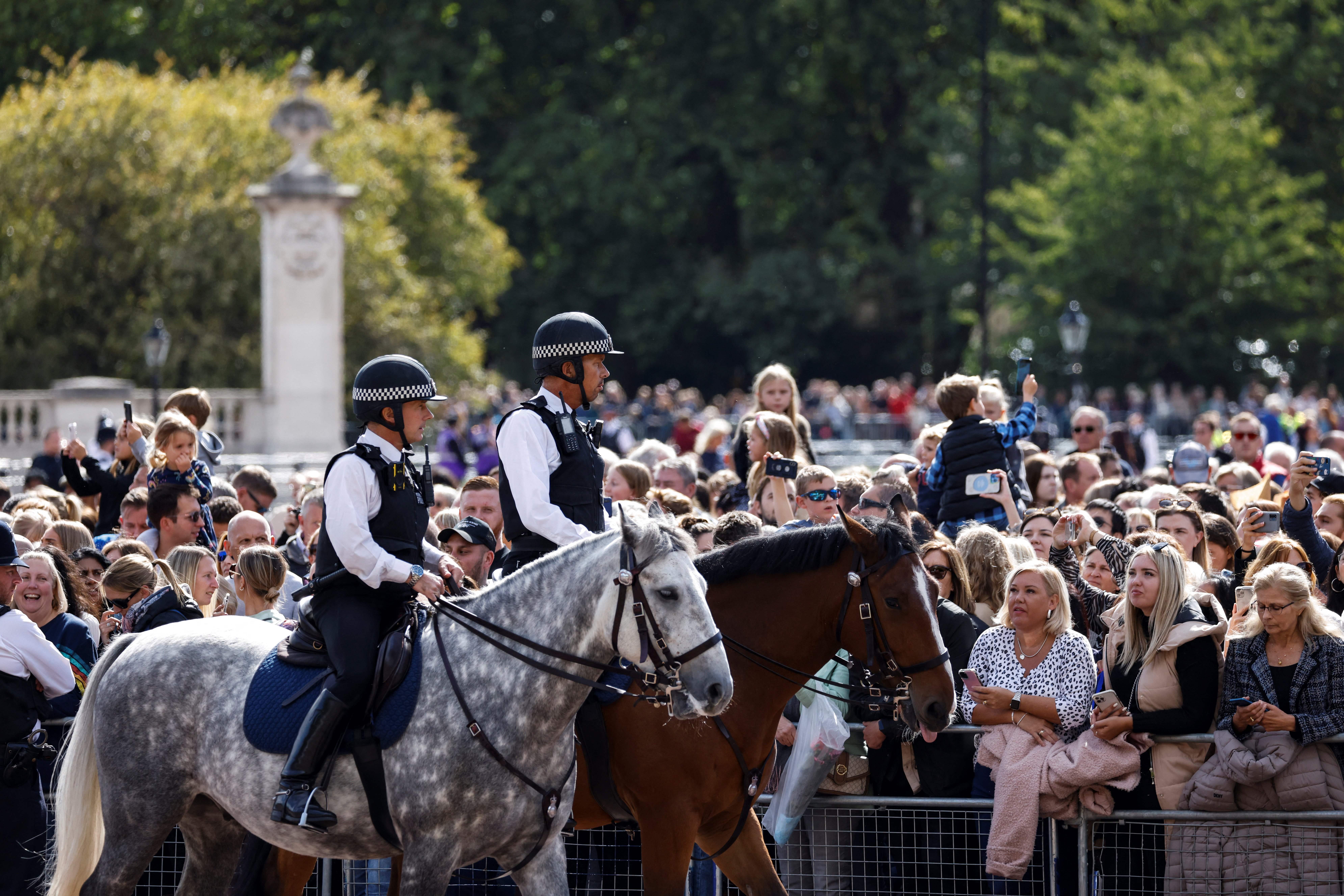 Police officers patrol on their horses as members of the public gather outside of Buckingham Palace on Sunday.