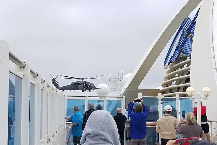 In this photo provided by Michele Smith, passengers look on as a Coast Guard helicopter hovers above the Grand Princess cruise ship on Thursday, March 5, off the California coast. 
