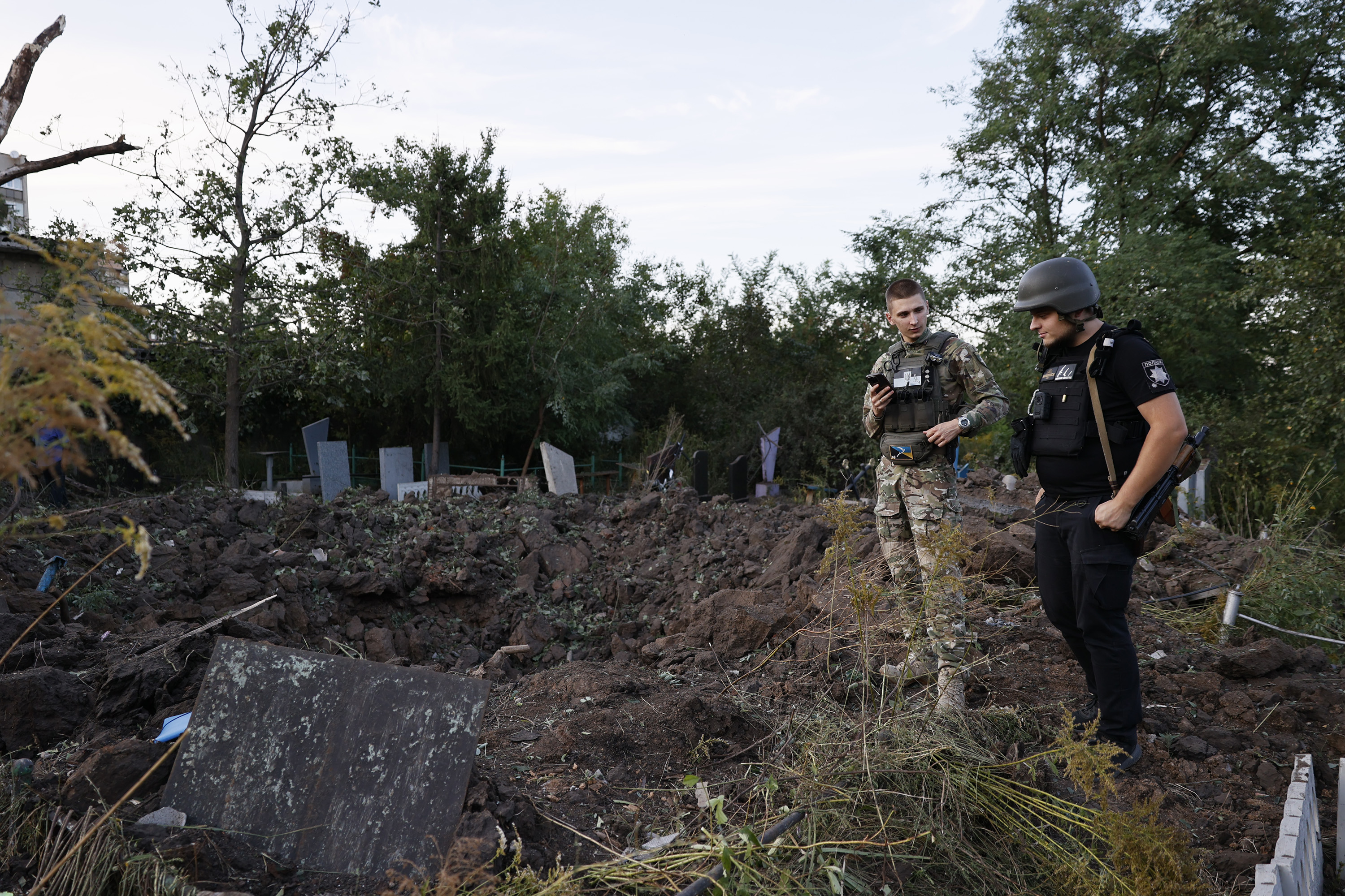 Ukrainian military member with policeman stand near hole left by missile on September 2, in Kramatorsk, Donetsk region.