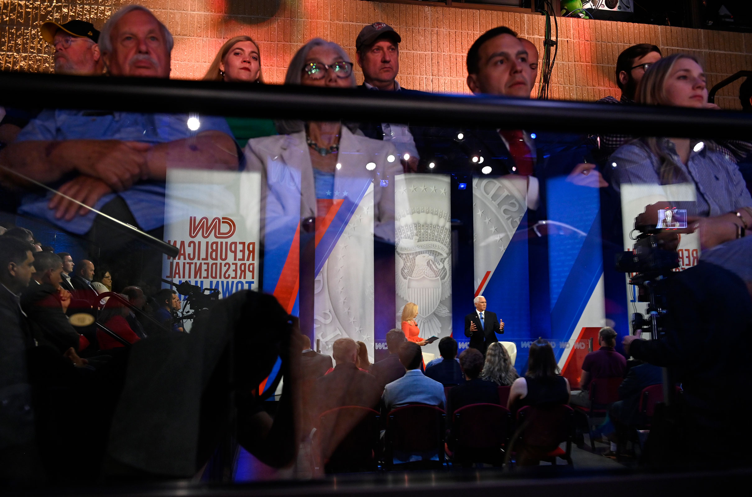 Mike Pence, reflected in the glass, participates in the town hall as audience members listen. 
