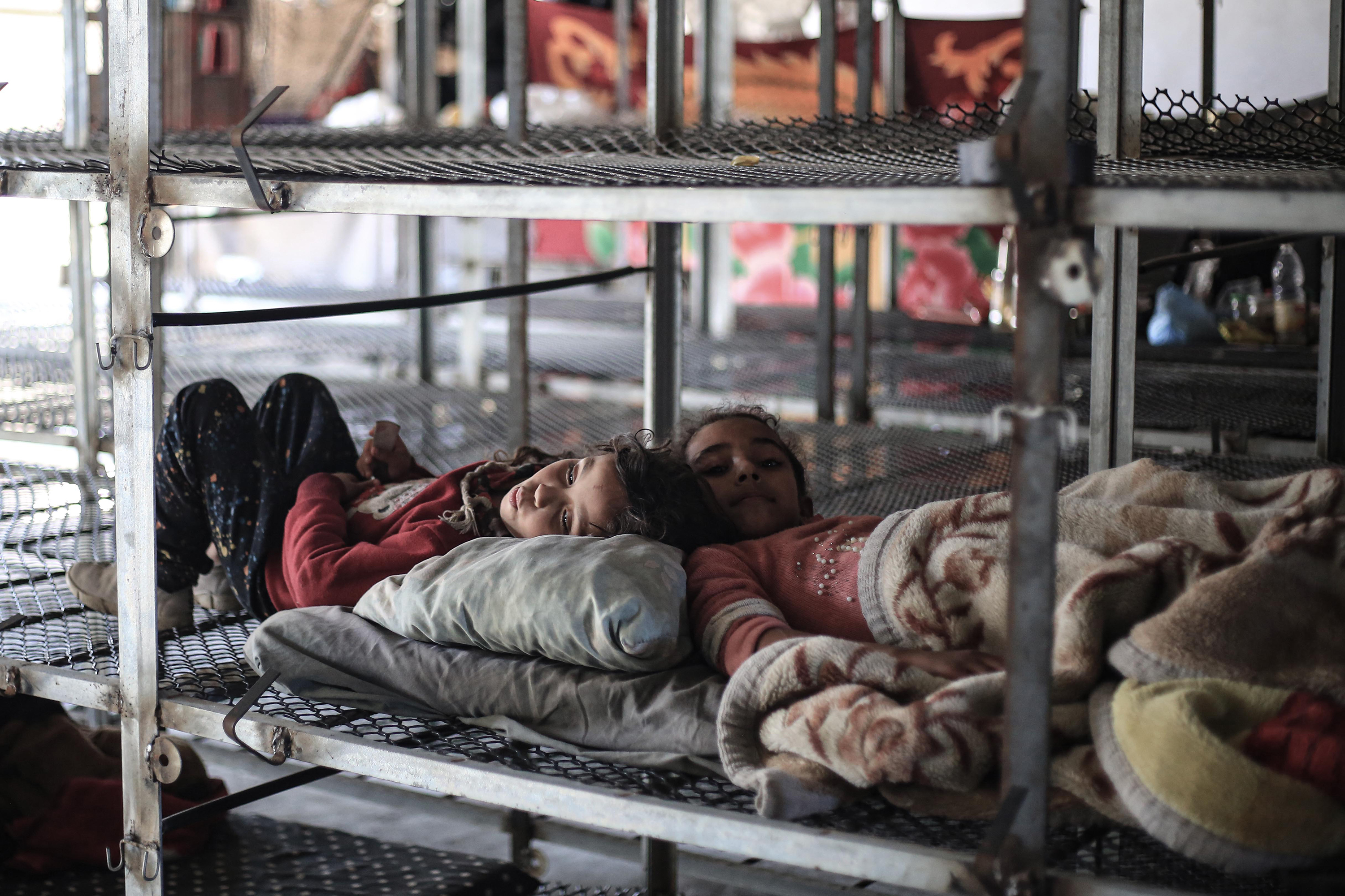 Due to a lack of a tent, displaced Palestinian children rest while residing with their families inside a poultry farm.