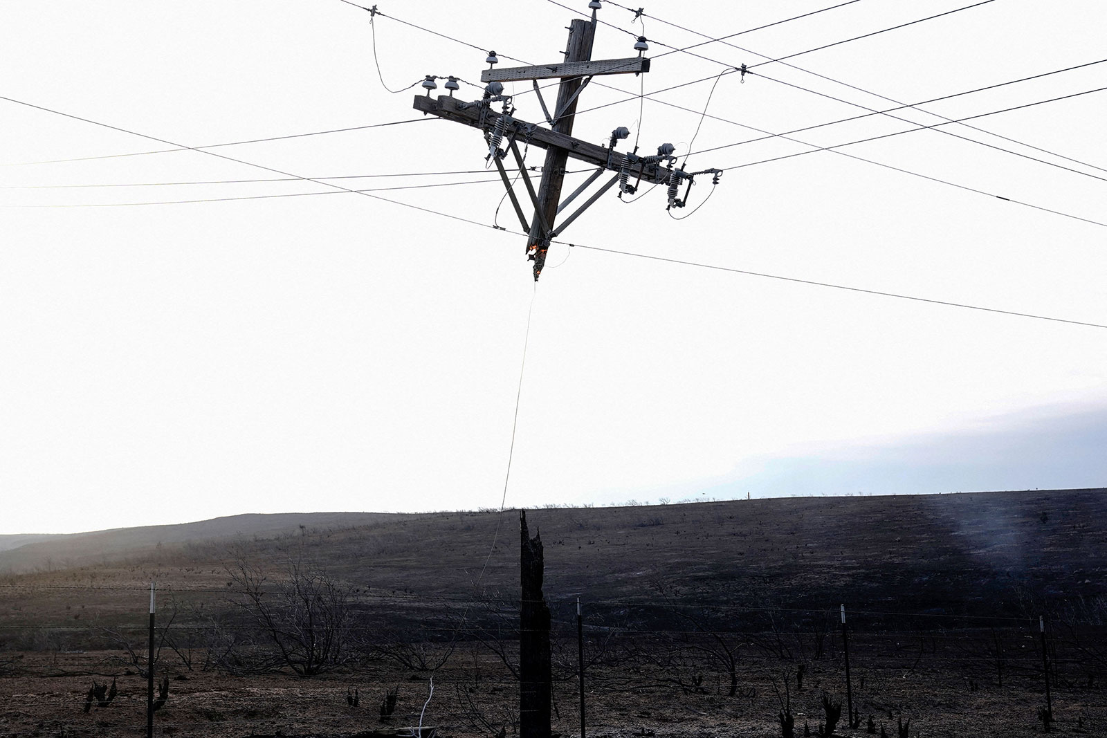 A burned power pole hangs from power lines.