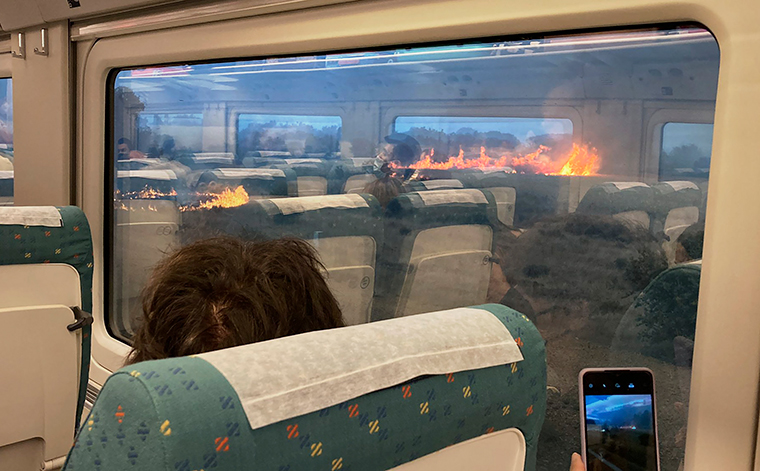 Passengers take photos at a wildfire while traveling on a train in Zamora, Spain, Monday, July 18, 2022. Francisco Seoane told The Associated Press it was scary to see how quickly the fire spread. Video of the unscheduled stop shows about a dozen passengers in Seoane's railcar appearing alarmed as they look out of the windows Monday, July 18. 